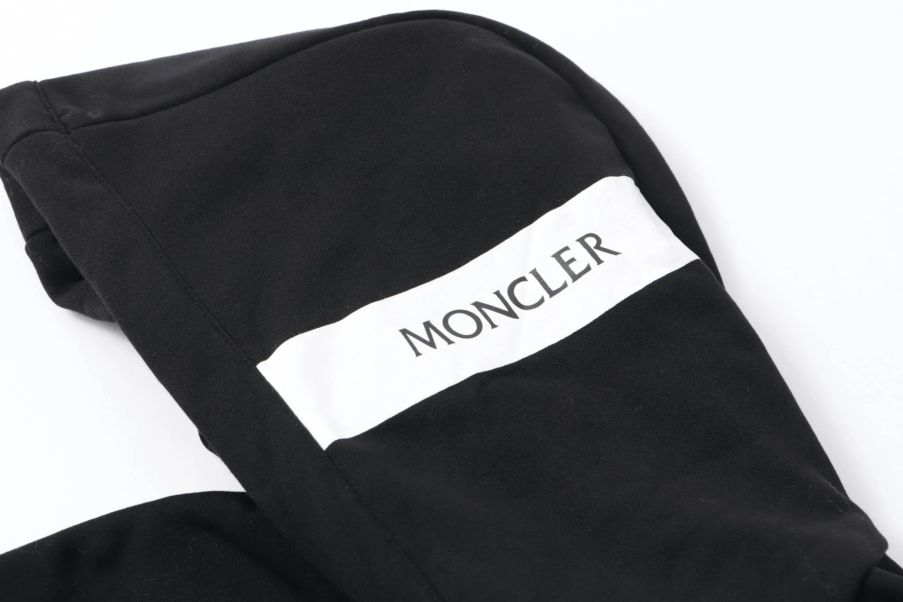 P340 Moncler slogan printed zipper hooded jacket is made of lightweight turned velvet cotton fabric. High-density cotton fiber is used to achieve internal and external differentiation in a single layer of fabric. The outer plain weave is tight and wear-resistant, and the inner layer is sanded to form a short dense suede surface. The dense plain weave structure resists wind and splashes, the brushed suede surface is skin-friendly, and the short pile has been treated to eliminate static electricity to avoid sticking to the skin. A very small amount of grooved polyester moisture-conducting yarn is embedded in the cotton fiber, which quickly guides sweat from the inner suede surface to the outer layer for evaporation through the capillary effect, solving the problem of the suede being easily stuffy. By actively interfering with the shrinkage potential of cotton fibers, the fabric is able to transition from changeable to stable, improving dimensional stability while being less prone to deformation and wrinkles. High saturation is achieved on the center of the cap through glue printing. Size: xs-l