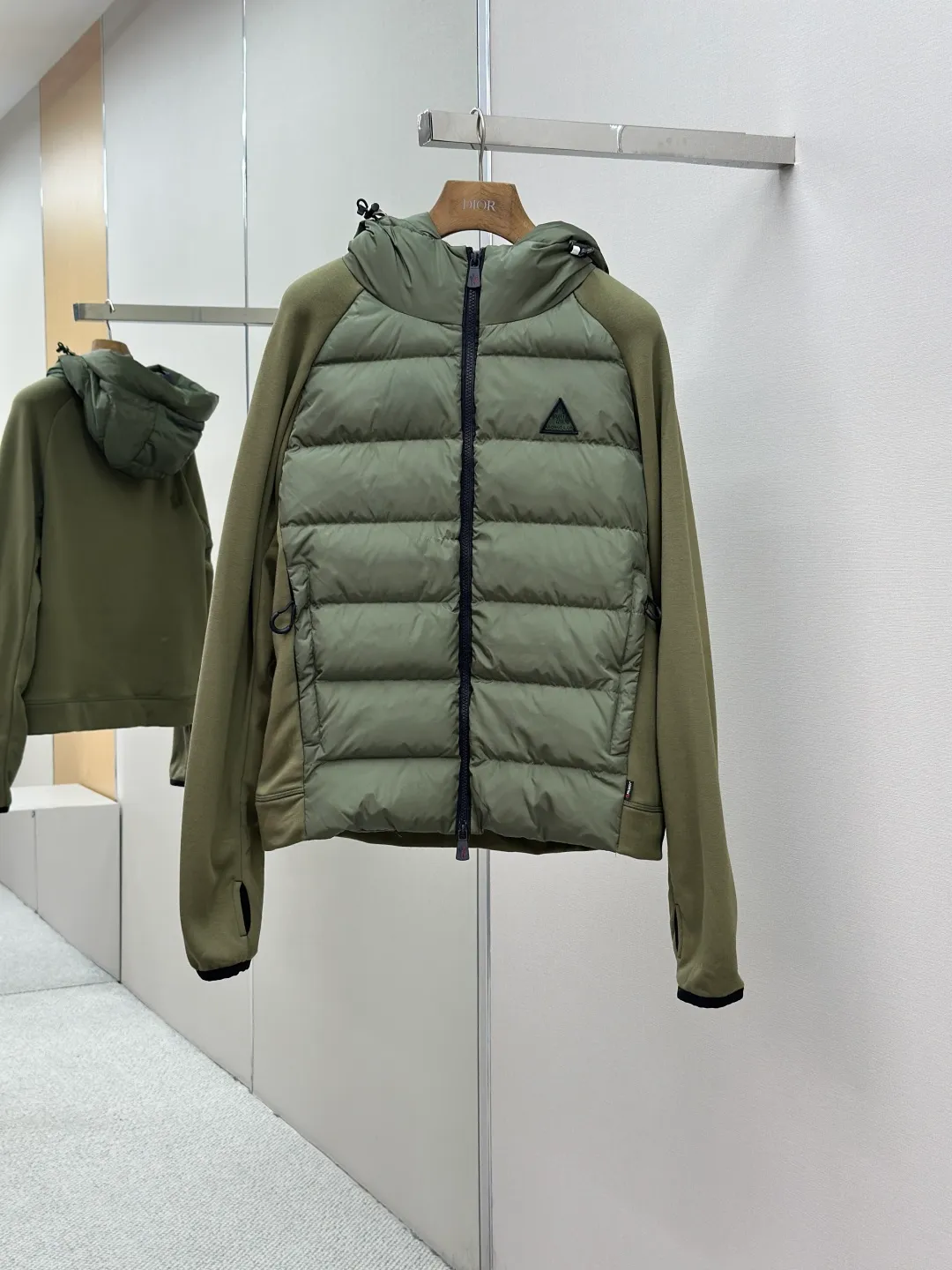 P810 Moncler logo woven splicing down jacket, customized matte crystal lattice air shield velvet and 300D high-density calendered coating, using the new national standard 90 white duck down (welcome to test), full of down, full of warmth, light and fluffy, with the dark green of the overlapping mountains as the background color, all things accumulating, creating its own scenery in silence The Monlcer triangle logo is embellished on the chest, the power aesthetics of the minimalist logo The concentrated down filling in the front area creates dynamic insulation for the core heat dissipation zone of the human body. The hooded down is a moving warm flow barrier for the head and neck, forming a thermal energy circulation system with the front area. The elastic woven sleeves provide freedom of movement with a sense of compression, forming a relaxed and warm philosophy. The real high-end is to let function become the footnote of style. Process 1: Computer mechanical down filling. Prioritize the liner pattern by making a pattern to determine the down filling area and determine the weight of down per square meter according to the original three-dimensional effect. Thus, the amount of down filling for each cut piece is calculated. The computer down filling machine uses a digital weighing unit to achieve stable measurement. Process 2: 3D three-dimensional quilting technology. With the programming system of the CNC quilting machine, the down in different areas is accurately separated to ensure that the filling is evenly fixed after sewing and avoid agglomeration or displacement. Process 3: Computer template machine line running process. The computer template machine line line process shows extremely high neatness and smoothness. The craftsman's precise control of the size during the operation ensures that each line meets the design requirements. The lines of the entire template are smooth and unified, neat and beautiful. Process 4: Triple locking five-thread dense stitching process. Main seam locking + diagonal reinforcement + raw edge wrapping. Triple structure. Forming a three-dimensional protective net at the edge of the fabric to avoid stitch breakage. Paving materials: Customized Moncler zippers. Customized Moncler rope loops. Customized Moncler logo. Customized Moncler eyelets. Customized Moncler trademark. Size: S M L XL