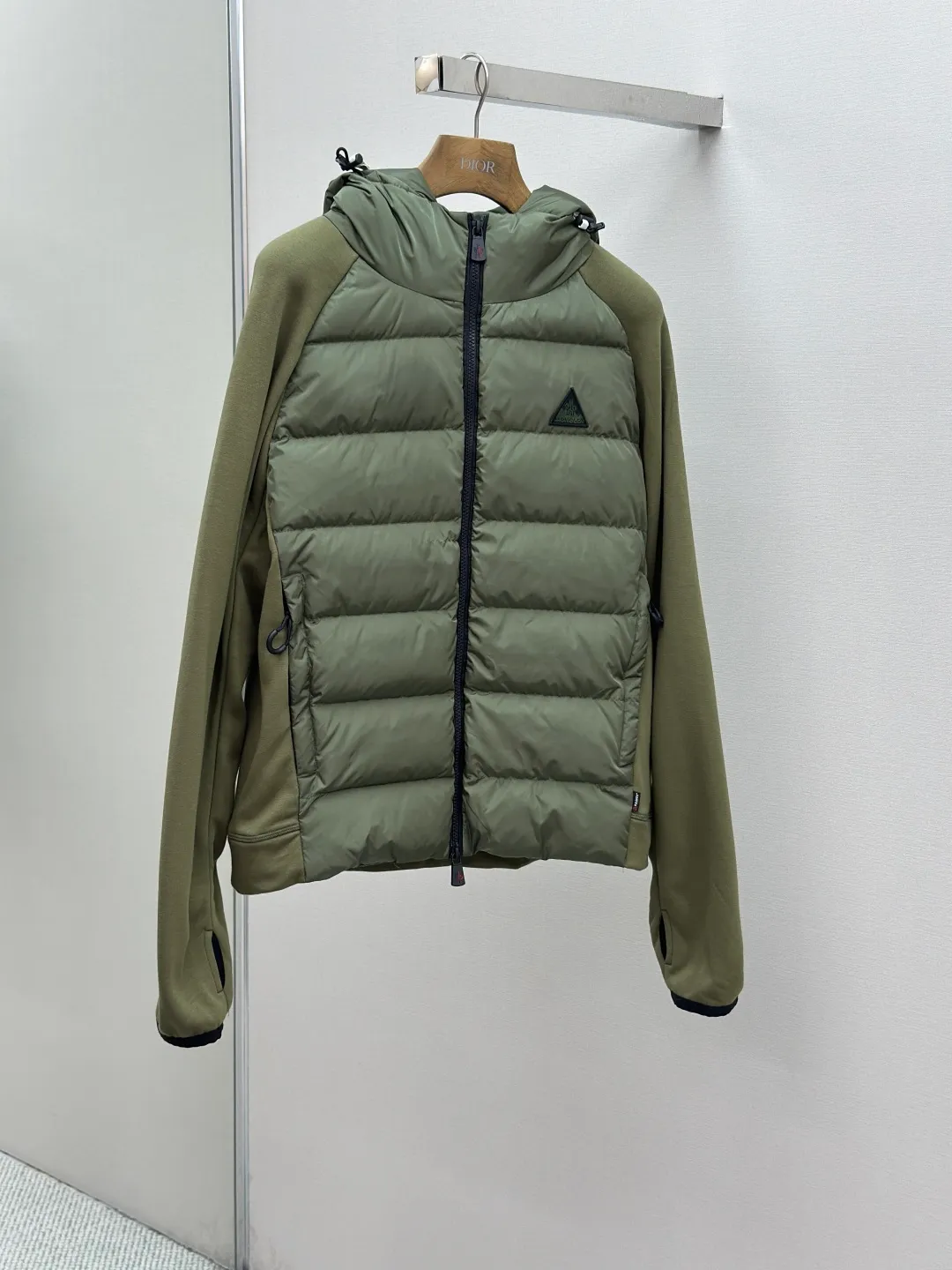 P810 Moncler logo woven splicing down jacket, customized matte crystal lattice air shield velvet and 300D high-density calendered coating, using the new national standard 90 white duck down (welcome to test), full of down, full of warmth, light and fluffy, with the dark green of the overlapping mountains as the background color, all things accumulating, creating its own scenery in silence The Monlcer triangle logo is embellished on the chest, the power aesthetics of the minimalist logo The concentrated down filling in the front area creates dynamic insulation for the core heat dissipation zone of the human body. The hooded down is a moving warm flow barrier for the head and neck, forming a thermal energy circulation system with the front area. The elastic woven sleeves provide freedom of movement with a sense of compression, forming a relaxed and warm philosophy. The real high-end is to let function become the footnote of style. Process 1: Computer mechanical down filling. Prioritize the liner pattern by making a pattern to determine the down filling area and determine the weight of down per square meter according to the original three-dimensional effect. Thus, the amount of down filling for each cut piece is calculated. The computer down filling machine uses a digital weighing unit to achieve stable measurement. Process 2: 3D three-dimensional quilting technology. With the programming system of the CNC quilting machine, the down in different areas is accurately separated to ensure that the filling is evenly fixed after sewing and avoid agglomeration or displacement. Process 3: Computer template machine line running process. The computer template machine line line process shows extremely high neatness and smoothness. The craftsman's precise control of the size during the operation ensures that each line meets the design requirements. The lines of the entire template are smooth and unified, neat and beautiful. Process 4: Triple locking five-thread dense stitching process. Main seam locking + diagonal reinforcement + raw edge wrapping. Triple structure. Forming a three-dimensional protective net at the edge of the fabric to avoid stitch breakage. Paving materials: Customized Moncler zippers. Customized Moncler rope loops. Customized Moncler logo. Customized Moncler eyelets. Customized Moncler trademark. Size: S M L XL