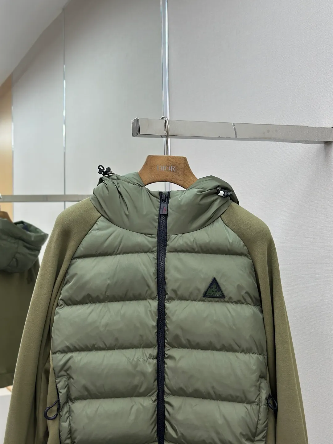 P810 Moncler logo woven splicing down jacket, customized matte crystal lattice air shield velvet and 300D high-density calendered coating, using the new national standard 90 white duck down (welcome to test), full of down, full of warmth, light and fluffy, with the dark green of the overlapping mountains as the background color, all things accumulating, creating its own scenery in silence The Monlcer triangle logo is embellished on the chest, the power aesthetics of the minimalist logo The concentrated down filling in the front area creates dynamic insulation for the core heat dissipation zone of the human body. The hooded down is a moving warm flow barrier for the head and neck, forming a thermal energy circulation system with the front area. The elastic woven sleeves provide freedom of movement with a sense of compression, forming a relaxed and warm philosophy. The real high-end is to let function become the footnote of style. Process 1: Computer mechanical down filling. Prioritize the liner pattern by making a pattern to determine the down filling area and determine the weight of down per square meter according to the original three-dimensional effect. Thus, the amount of down filling for each cut piece is calculated. The computer down filling machine uses a digital weighing unit to achieve stable measurement. Process 2: 3D three-dimensional quilting technology. With the programming system of the CNC quilting machine, the down in different areas is accurately separated to ensure that the filling is evenly fixed after sewing and avoid agglomeration or displacement. Process 3: Computer template machine line running process. The computer template machine line line process shows extremely high neatness and smoothness. The craftsman's precise control of the size during the operation ensures that each line meets the design requirements. The lines of the entire template are smooth and unified, neat and beautiful. Process 4: Triple locking five-thread dense stitching process. Main seam locking + diagonal reinforcement + raw edge wrapping. Triple structure. Forming a three-dimensional protective net at the edge of the fabric to avoid stitch breakage. Paving materials: Customized Moncler zippers. Customized Moncler rope loops. Customized Moncler logo. Customized Moncler eyelets. Customized Moncler trademark. Size: S M L XL