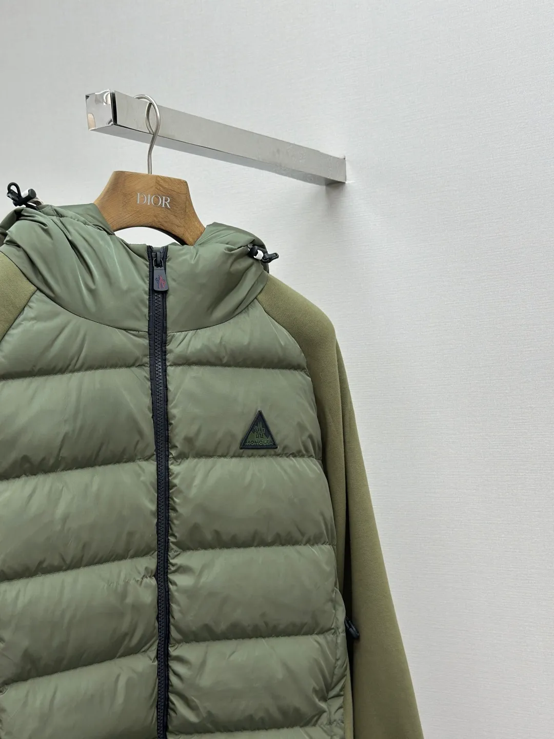P810 Moncler logo woven splicing down jacket, customized matte crystal lattice air shield velvet and 300D high-density calendered coating, using the new national standard 90 white duck down (welcome to test), full of down, full of warmth, light and fluffy, with the dark green of the overlapping mountains as the background color, all things accumulating, creating its own scenery in silence The Monlcer triangle logo is embellished on the chest, the power aesthetics of the minimalist logo The concentrated down filling in the front area creates dynamic insulation for the core heat dissipation zone of the human body. The hooded down is a moving warm flow barrier for the head and neck, forming a thermal energy circulation system with the front area. The elastic woven sleeves provide freedom of movement with a sense of compression, forming a relaxed and warm philosophy. The real high-end is to let function become the footnote of style. Process 1: Computer mechanical down filling. Prioritize the liner pattern by making a pattern to determine the down filling area and determine the weight of down per square meter according to the original three-dimensional effect. Thus, the amount of down filling for each cut piece is calculated. The computer down filling machine uses a digital weighing unit to achieve stable measurement. Process 2: 3D three-dimensional quilting technology. With the programming system of the CNC quilting machine, the down in different areas is accurately separated to ensure that the filling is evenly fixed after sewing and avoid agglomeration or displacement. Process 3: Computer template machine line running process. The computer template machine line line process shows extremely high neatness and smoothness. The craftsman's precise control of the size during the operation ensures that each line meets the design requirements. The lines of the entire template are smooth and unified, neat and beautiful. Process 4: Triple locking five-thread dense stitching process. Main seam locking + diagonal reinforcement + raw edge wrapping. Triple structure. Forming a three-dimensional protective net at the edge of the fabric to avoid stitch breakage. Paving materials: Customized Moncler zippers. Customized Moncler rope loops. Customized Moncler logo. Customized Moncler eyelets. Customized Moncler trademark. Size: S M L XL