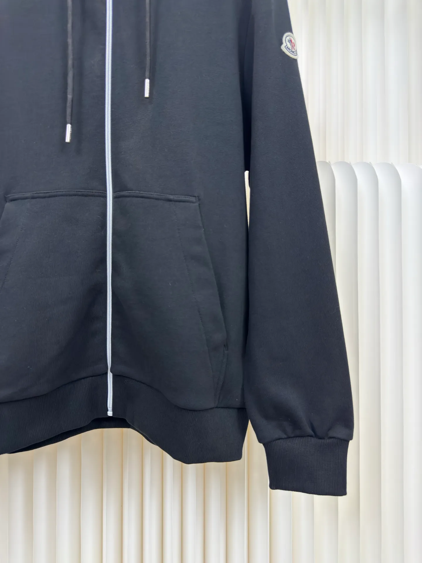 P500 MONCLER printed logo hooded sweatshirt is made of lightweight turned-over velvet cotton fabric. High-density cotton fiber is used to achieve internal and external differentiation in a single layer of fabric. The outer plain weave is tight and wear-resistant, and the inner layer is sanded to form a short dense suede surface. The dense plain weave structure resists wind and splashes, the brushed suede surface is skin-friendly, and the short pile has been treated to eliminate static electricity to avoid sticking to the skin. A very small amount of grooved polyester moisture-conducting yarn is embedded in the cotton fiber, which quickly directs sweat from the inner suede surface to the outer layer for evaporation through the capillary effect, solving the problem that the inside-out suede is prone to stuffiness. By actively intervening in the shrinkage potential of the cotton fiber, the fabric is achieved from being volatile to stable, improving dimensional stability, and at the same time not prone to deformation and wrinkles.   A high-saturation pattern is displayed on the center of the cap through glue printing. The scraper pressure is even and the scraping is performed in 5 steps to ensure that the glue is fully penetrated and covered. After curing at high temperature, the pigment is firmly combined with the cotton fiber. The ink absorption and penetration characteristics of the cotton fiber make the pattern less likely to fall off due to friction. Size S M L XL