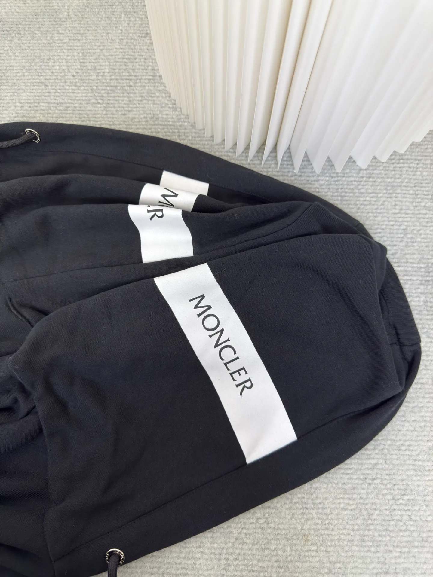 P500 MONCLER printed logo hooded sweatshirt is made of lightweight turned-over velvet cotton fabric. High-density cotton fiber is used to achieve internal and external differentiation in a single layer of fabric. The outer plain weave is tight and wear-resistant, and the inner layer is sanded to form a short dense suede surface. The dense plain weave structure resists wind and splashes, the brushed suede surface is skin-friendly, and the short pile has been treated to eliminate static electricity to avoid sticking to the skin. A very small amount of grooved polyester moisture-conducting yarn is embedded in the cotton fiber, which quickly directs sweat from the inner suede surface to the outer layer for evaporation through the capillary effect, solving the problem that the inside-out suede is prone to stuffiness. By actively intervening in the shrinkage potential of the cotton fiber, the fabric is achieved from being volatile to stable, improving dimensional stability, and at the same time not prone to deformation and wrinkles.   A high-saturation pattern is displayed on the center of the cap through glue printing. The scraper pressure is even and the scraping is performed in 5 steps to ensure that the glue is fully penetrated and covered. After curing at high temperature, the pigment is firmly combined with the cotton fiber. The ink absorption and penetration characteristics of the cotton fiber make the pattern less likely to fall off due to friction. Size S M L XL