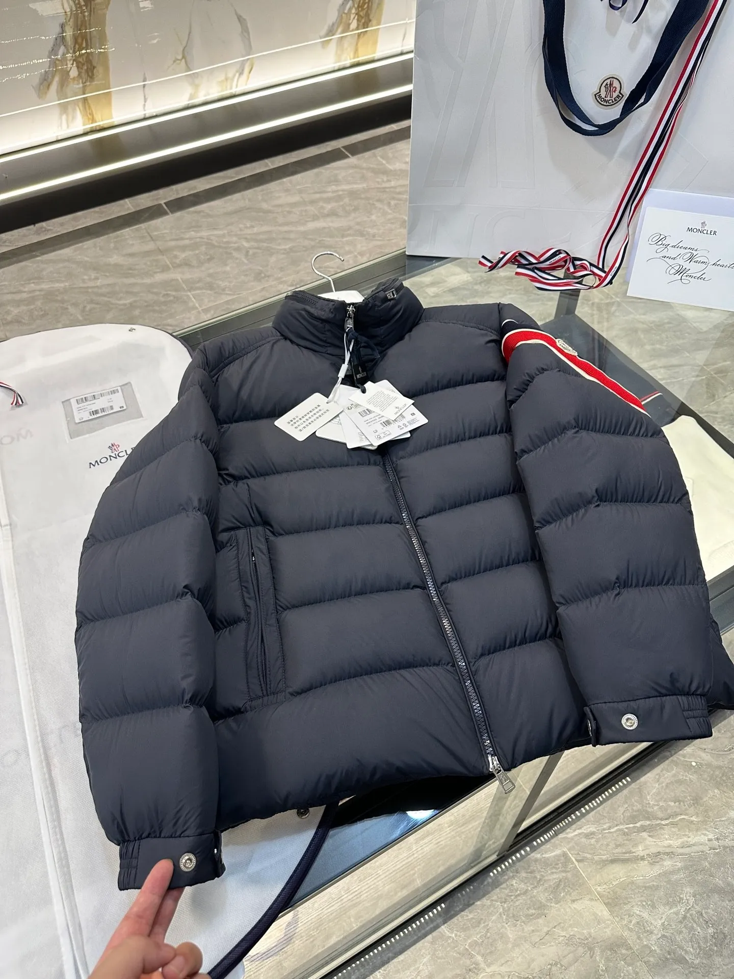 P920 2024N haute couture down moncler solayan men's three-color trimmed short down. Premium goose down filling. The most delicate, lightest and neatest fabric. Solayan men's short down is decorated with seasonal iconic stripe details, blending sportsmanship and timeless style. Solayan down is made of micro chic fabric and has a tough square shape design, highlighting Moncler's sporty spirit. This cropped style has tricolor stripes on the sleeves, a seasonal take on the brand's signature. Comes with a practical pull-out hood. Details · Made of micro chic nylon fabric · Micro chic nylon lining · Filled down · Pull-out hood · Zipper closure · Zipper pocket · Adjustable cuffs · Elastic drawstring hem · Tri-color trim on sleeves size: 1-5 Color: white, dark brown, black