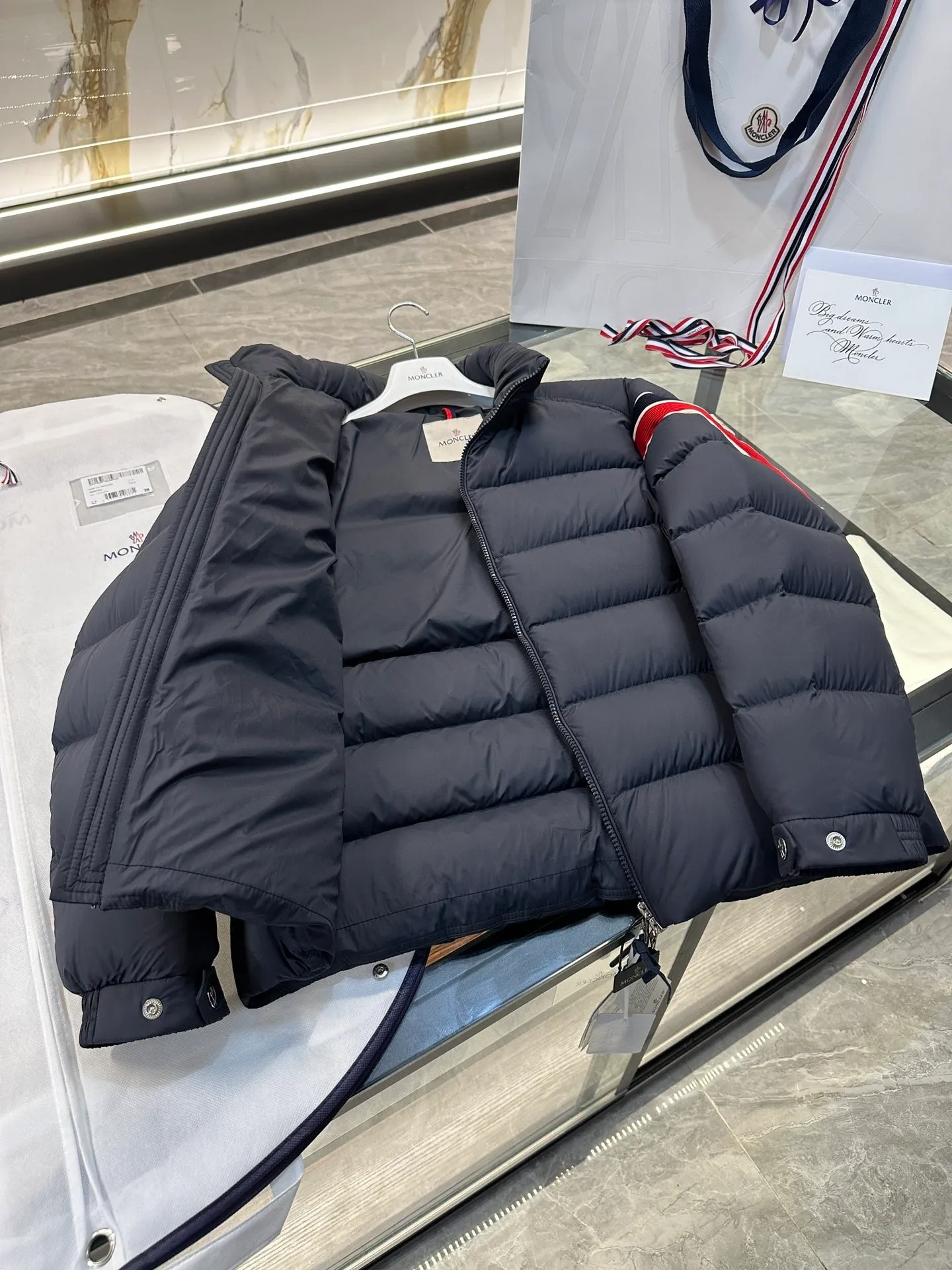 P920 2024N haute couture down moncler solayan men's three-color trimmed short down. Premium goose down filling. The most delicate, lightest and neatest fabric. Solayan men's short down is decorated with seasonal iconic stripe details, blending sportsmanship and timeless style. Solayan down is made of micro chic fabric and has a tough square shape design, highlighting Moncler's sporty spirit. This cropped style has tricolor stripes on the sleeves, a seasonal take on the brand's signature. Comes with a practical pull-out hood. Details · Made of micro chic nylon fabric · Micro chic nylon lining · Filled down · Pull-out hood · Zipper closure · Zipper pocket · Adjustable cuffs · Elastic drawstring hem · Tri-color trim on sleeves size: 1-5 Color: white, dark brown, black