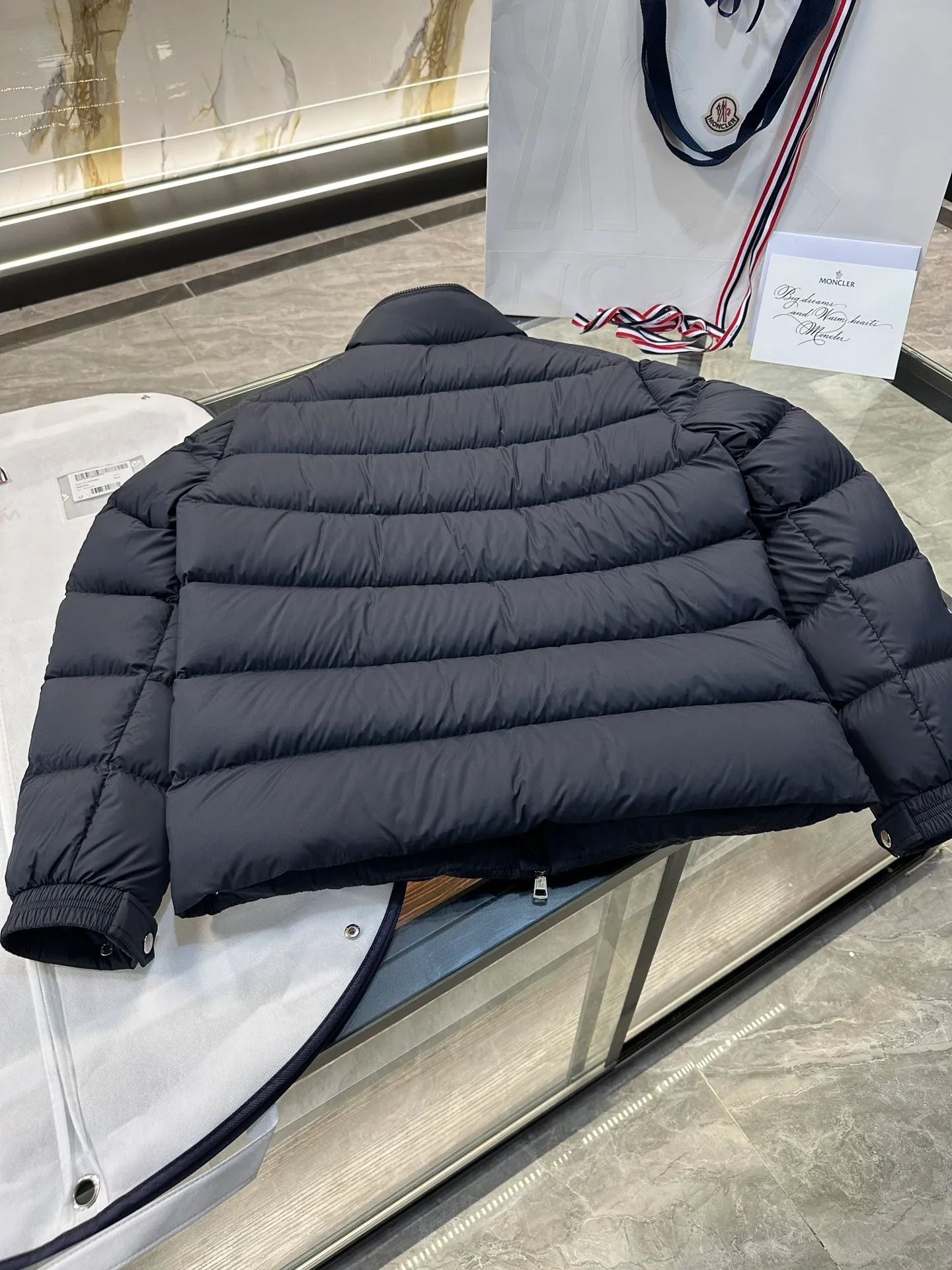 P920 2024N haute couture down moncler solayan men's three-color trimmed short down. Premium goose down filling. The most delicate, lightest and neatest fabric. Solayan men's short down is decorated with seasonal iconic stripe details, blending sportsmanship and timeless style. Solayan down is made of micro chic fabric and has a tough square shape design, highlighting Moncler's sporty spirit. This cropped style has tricolor stripes on the sleeves, a seasonal take on the brand's signature. Comes with a practical pull-out hood. Details · Made of micro chic nylon fabric · Micro chic nylon lining · Filled down · Pull-out hood · Zipper closure · Zipper pocket · Adjustable cuffs · Elastic drawstring hem · Tri-color trim on sleeves size: 1-5 Color: white, dark brown, black