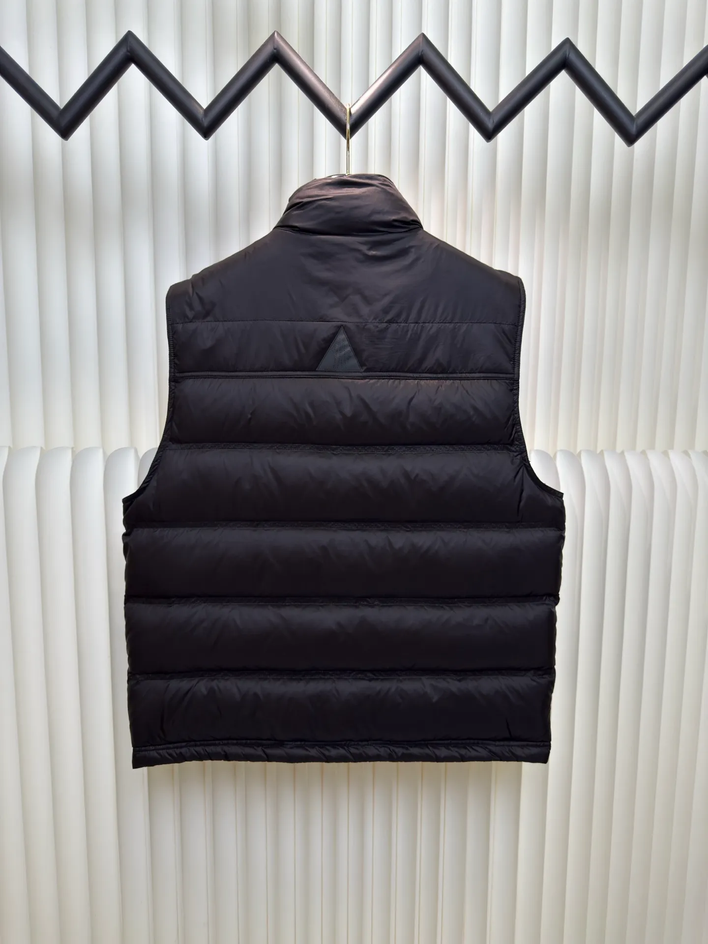 P700 MONCLER masked down vest with reflective markings is made of 90 white duck down with a weight of 130g to ensure excellent thermal insulation performance. After strict screening and processing, the velvet is not easy to get drilled, ensuring durability.  It is made of extremely fine nylon yarn and is woven in a high-density manner. The number of yarns per unit area is large, and the gaps between the yarns are very small, which can effectively block the penetration of cold wind. The fine weave keeps it lightweight and soft to the touch, physically restricting the lightweight down fibers from slipping through the gaps. Nylon fiber itself has good wear resistance and is not easy to snag, which significantly extends its service life and can easily cope with the needs of multiple scenarios.  The lining is made of high-density weaving of 100% polyester fiber, with a thickness of 0.08mm to avoid increasing the overall weight and making it smooth to wear. The high-density weaving structure forms a wind resistance layer to protect the thermal efficiency of the thermal layer from loss. It can withstand the expansion pressure of down and prevent deformation and damage after long-term use.  Through the reflective cloth punching process, the logo is regularly arranged on the triangular reflective mark with dozens of small holes, which not only improves functionality but also enhances recognition and aesthetics. Size 1 2 3 4