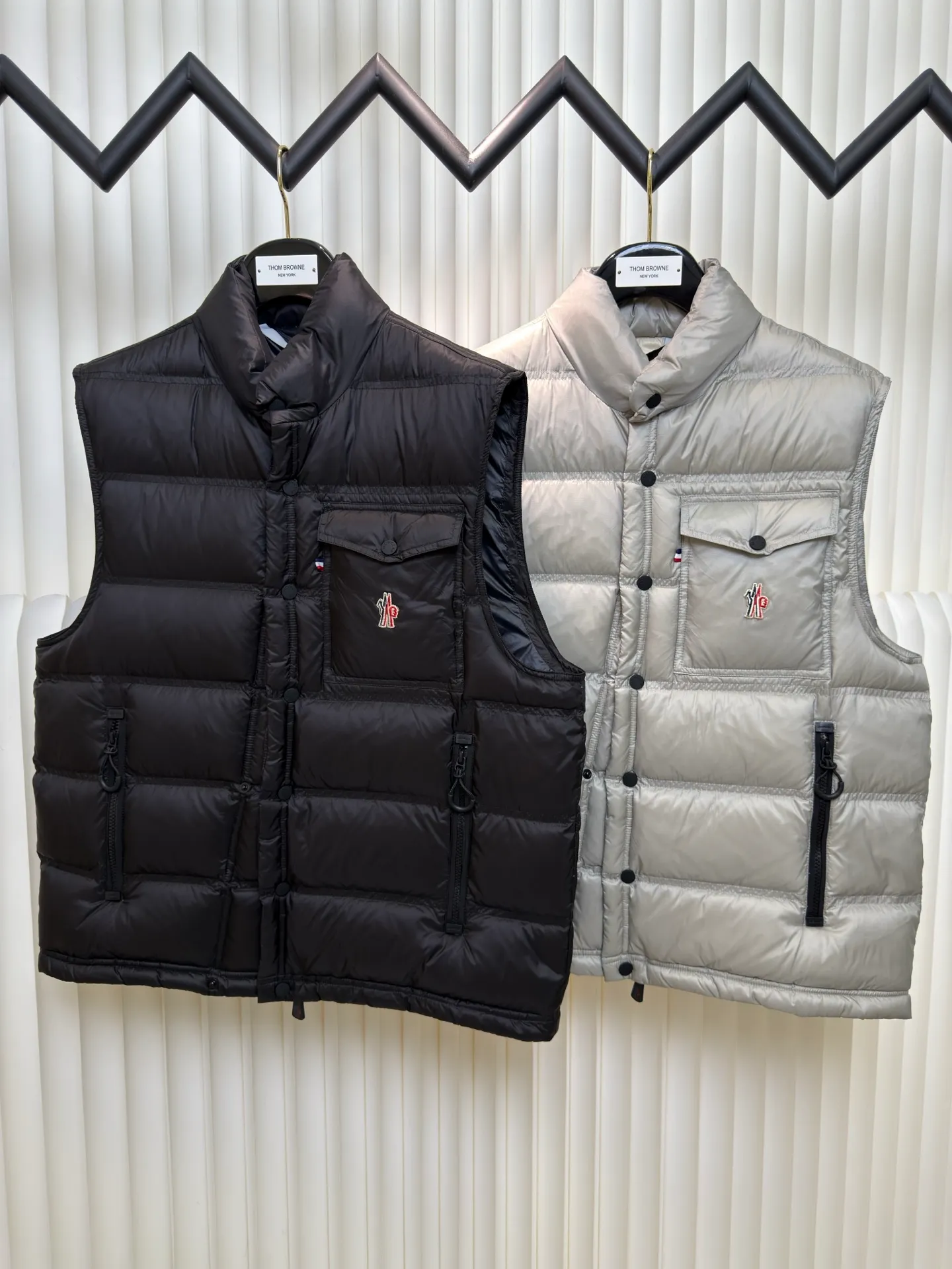 P700 MONCLER masked down vest with reflective markings is made of 90 white duck down with a weight of 130g to ensure excellent thermal insulation performance. After strict screening and processing, the velvet is not easy to get drilled, ensuring durability.  It is made of extremely fine nylon yarn and is woven in a high-density manner. The number of yarns per unit area is large, and the gaps between the yarns are very small, which can effectively block the penetration of cold wind. The fine weave keeps it lightweight and soft to the touch, physically restricting the lightweight down fibers from slipping through the gaps. Nylon fiber itself has good wear resistance and is not easy to snag, which significantly extends its service life and can easily cope with the needs of multiple scenarios.  The lining is made of high-density weaving of 100% polyester fiber, with a thickness of 0.08mm to avoid increasing the overall weight and making it smooth to wear. The high-density weaving structure forms a wind resistance layer to protect the thermal efficiency of the thermal layer from loss. It can withstand the expansion pressure of down and prevent deformation and damage after long-term use.  Through the reflective cloth punching process, the logo is regularly arranged on the triangular reflective mark with dozens of small holes, which not only improves functionality but also enhances recognition and aesthetics. Size 1 2 3 4
