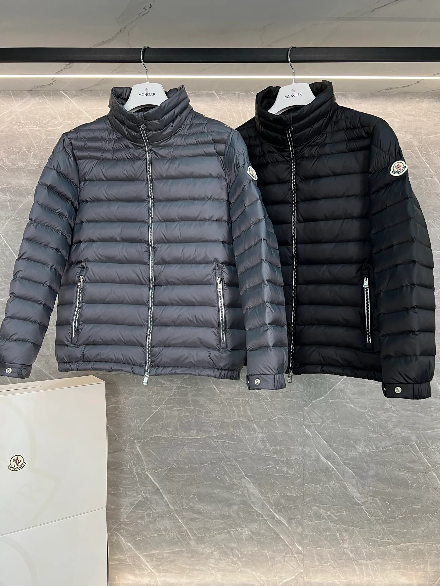 P780 Moncler Arnique short and lightweight men's down jacket. Super soft and delicate fabric, white duck down filling. Extremely lightweight and warm. The Arnique hooded down jacket is made of polyester fiber outer fabric and is Moncler's classic men's design item.  The Arnique short down jacket features classic checkered quilting and signature patch pockets on the sleeves, highlighting the Moncler style. The outer fabric reflects the brand's commitment to lowering its environmental footprint. Modular design, removable hood can be easily put on and taken off according to weather conditions. Details Made of polyester outer fabric Polyester lining Filled with down Size: 1-5 Silver Gray Black