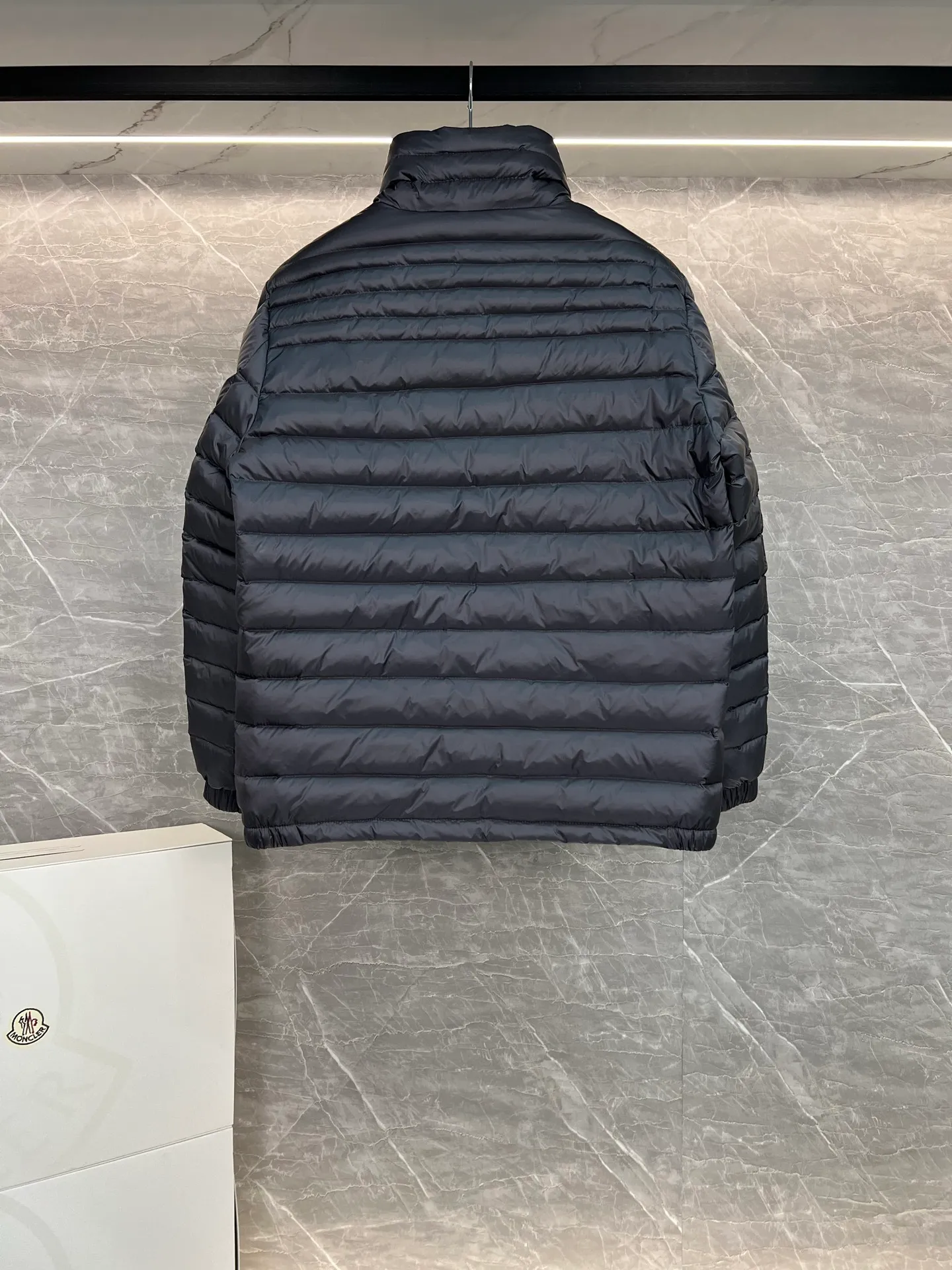 P780 Moncler Arnique short and lightweight men's down jacket. Super soft and delicate fabric, white duck down filling. Extremely lightweight and warm. The Arnique hooded down jacket is made of polyester fiber outer fabric and is Moncler's classic men's design item.  The Arnique short down jacket features classic checkered quilting and signature patch pockets on the sleeves, highlighting the Moncler style. The outer fabric reflects the brand's commitment to lowering its environmental footprint. Modular design, removable hood can be easily put on and taken off according to weather conditions. Details Made of polyester outer fabric Polyester lining Filled with down Size: 1-5 Silver Gray Black