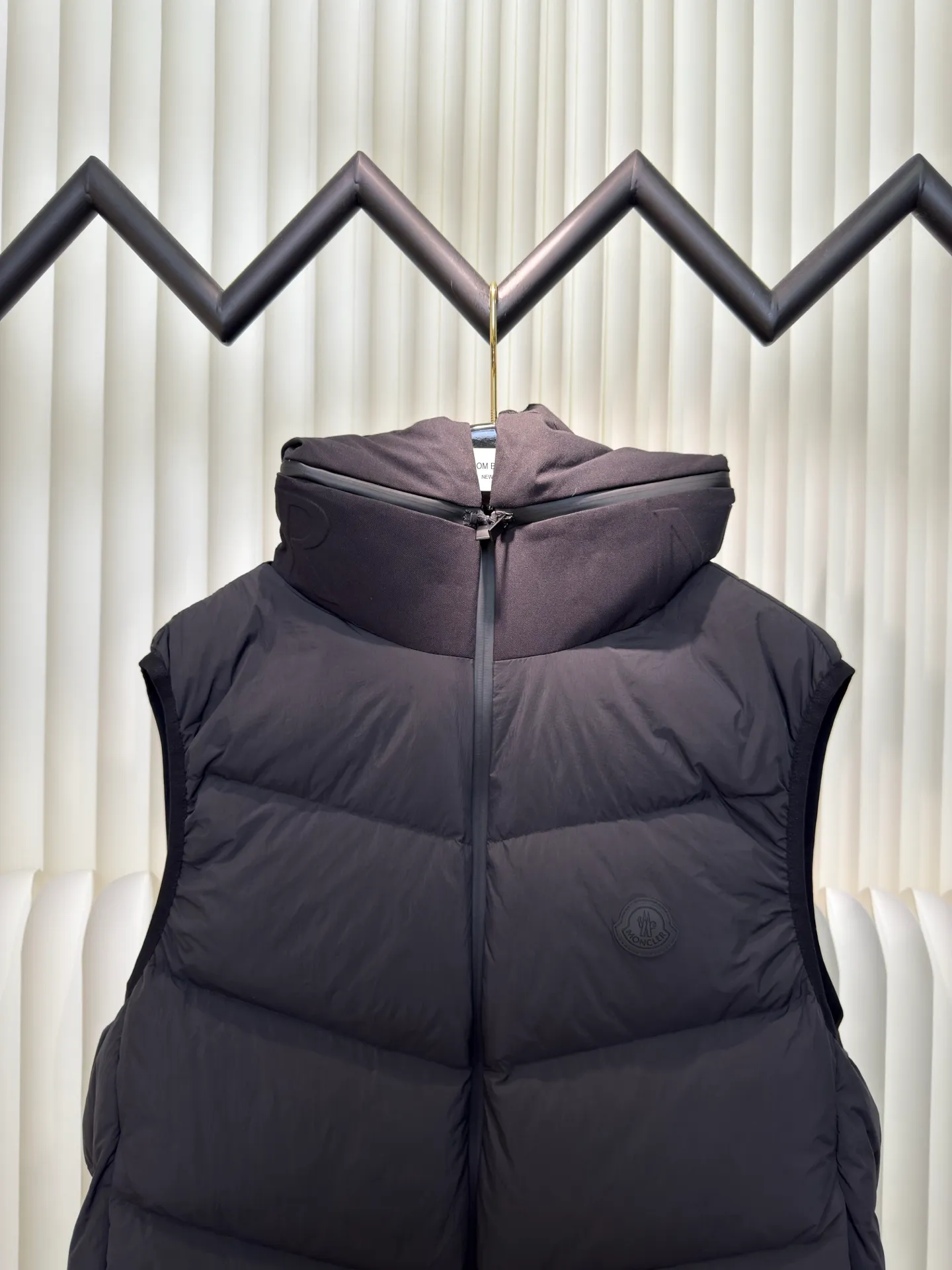P660 MONCLER Badge Hooded Down Vest is made of nylon fabric made of 100% nylon. It is woven into a tight and tough fabric through advanced textile technology. It improves the strength of the frame and effectively blocks the invasion of cold wind and locks in the warm air generated by the down layer. After tight weaving and special treatment, it is waterproof and windproof. The surface forms a certain lotus leaf effect. It is also wrinkle-resistant and not easy to deform, making it easy for daily care.  The quilting stitches are sewn in a diagonal direction at an angle of about 70 degrees, and the diagonal lines are arranged in parallel. The fabric and filling are planned into different functional areas, and the quilting stitches in each partition are relatively independent. This allows the finished product to produce a larger deformation space along the diagonal direction when stretched and pressed, making it less likely to tighten and break, and has rich visual effects, modern and advanced features.  After the hood is removed, the stand-up collar displays an embossed logo of the same color, adding a unique visual experience and tactile details. High-quality filling: It is filled with 90% selected white duck down, weighing 170g, ensuring fluffy rebound, lightness and warmth. Size 1 2 3 4