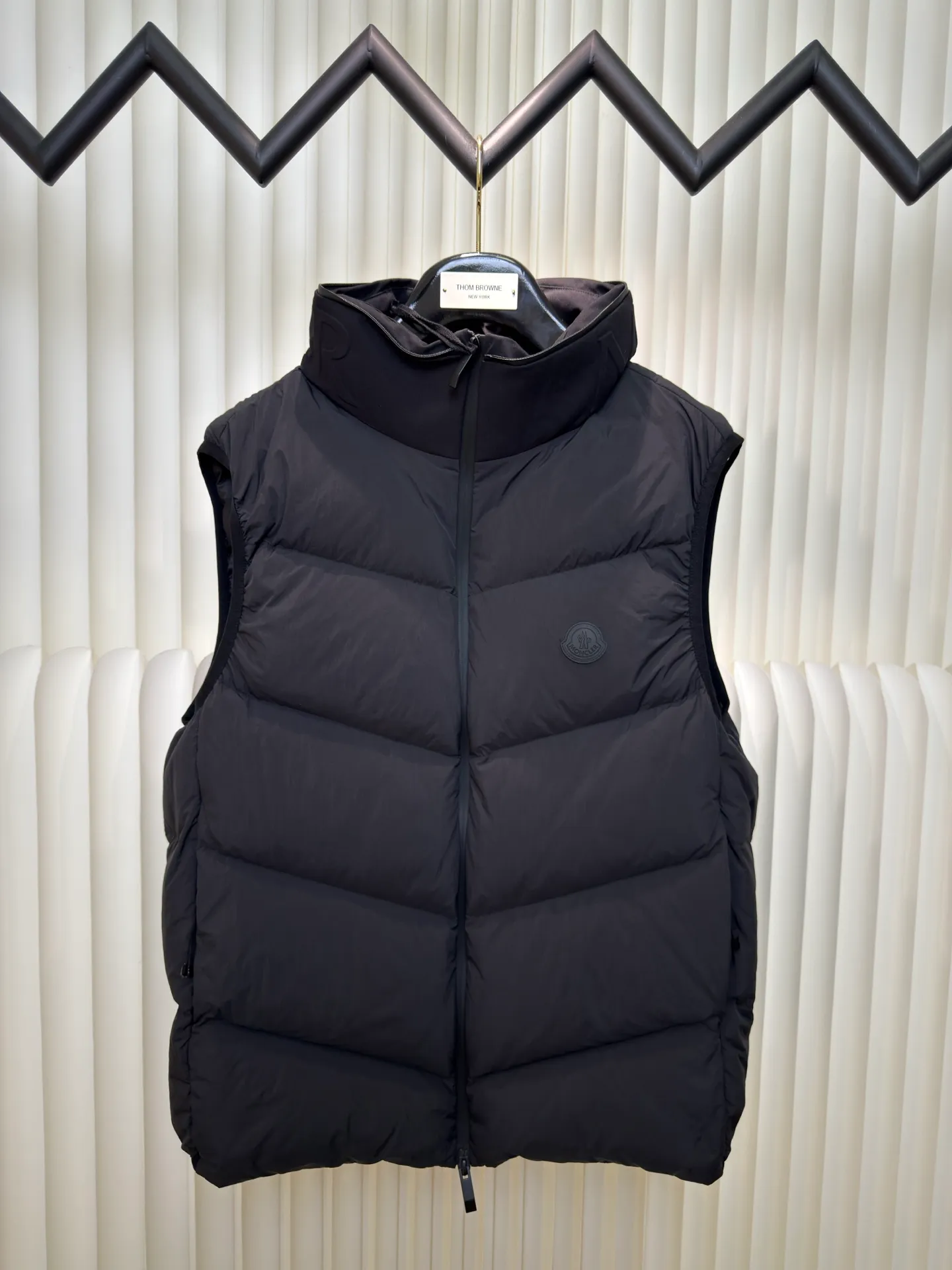 P660 MONCLER Badge Hooded Down Vest is made of nylon fabric made of 100% nylon. It is woven into a tight and tough fabric through advanced textile technology. It improves the strength of the frame and effectively blocks the invasion of cold wind and locks in the warm air generated by the down layer. After tight weaving and special treatment, it is waterproof and windproof. The surface forms a certain lotus leaf effect. It is also wrinkle-resistant and not easy to deform, making it easy for daily care.  The quilting stitches are sewn in a diagonal direction at an angle of about 70 degrees, and the diagonal lines are arranged in parallel. The fabric and filling are planned into different functional areas, and the quilting stitches in each partition are relatively independent. This allows the finished product to produce a larger deformation space along the diagonal direction when stretched and pressed, making it less likely to tighten and break, and has rich visual effects, modern and advanced features.  After the hood is removed, the stand-up collar displays an embossed logo of the same color, adding a unique visual experience and tactile details. High-quality filling: It is filled with 90% selected white duck down, weighing 170g, ensuring fluffy rebound, lightness and warmth. Size 1 2 3 4