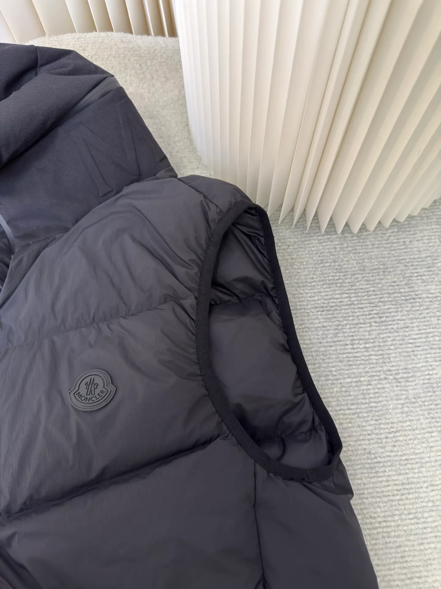 P660 MONCLER Badge Hooded Down Vest is made of nylon fabric made of 100% nylon. It is woven into a tight and tough fabric through advanced textile technology. It improves the strength of the frame and effectively blocks the invasion of cold wind and locks in the warm air generated by the down layer. After tight weaving and special treatment, it is waterproof and windproof. The surface forms a certain lotus leaf effect. It is also wrinkle-resistant and not easy to deform, making it easy for daily care.  The quilting stitches are sewn in a diagonal direction at an angle of about 70 degrees, and the diagonal lines are arranged in parallel. The fabric and filling are planned into different functional areas, and the quilting stitches in each partition are relatively independent. This allows the finished product to produce a larger deformation space along the diagonal direction when stretched and pressed, making it less likely to tighten and break, and has rich visual effects, modern and advanced features.  After the hood is removed, the stand-up collar displays an embossed logo of the same color, adding a unique visual experience and tactile details. High-quality filling: It is filled with 90% selected white duck down, weighing 170g, ensuring fluffy rebound, lightness and warmth. Size 1 2 3 4
