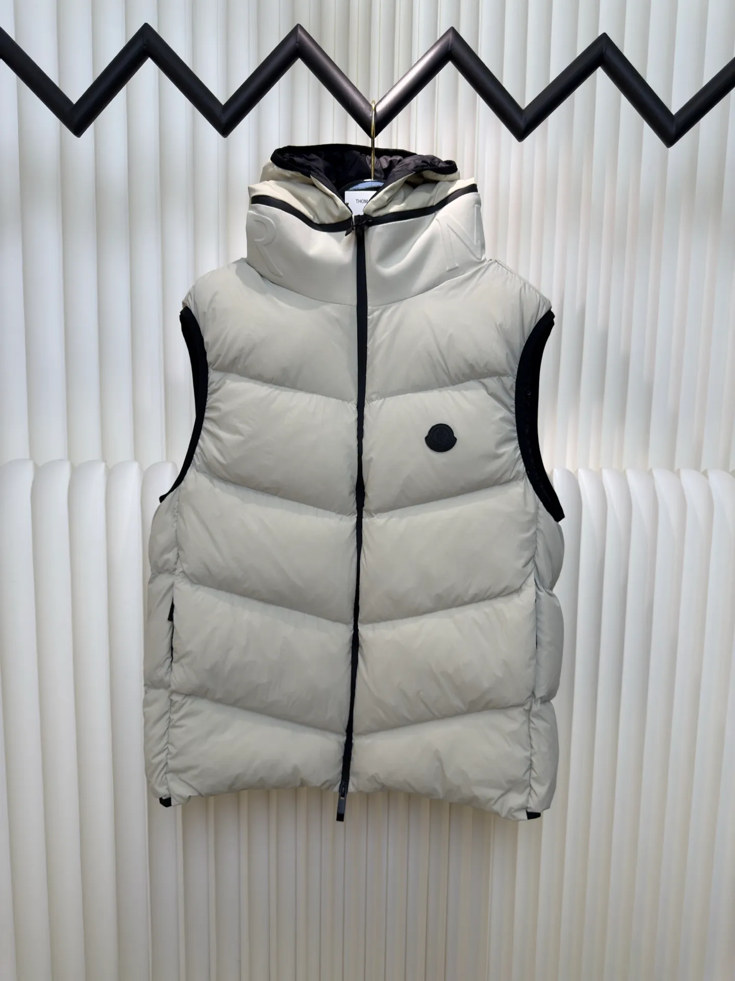 P660 MONCLER Badge Hooded Down Vest is made of nylon fabric made of 100% nylon. It is woven into a tight and tough fabric through advanced textile technology. It improves the strength of the frame and effectively blocks the invasion of cold wind and locks in the warm air generated by the down layer. After tight weaving and special treatment, it is waterproof and windproof. The surface forms a certain lotus leaf effect. It is also wrinkle-resistant and not easy to deform, making it easy for daily care.  The quilting stitches are sewn in a diagonal direction at an angle of about 70 degrees, and the diagonal lines are arranged in parallel. The fabric and filling are planned into different functional areas, and the quilting stitches in each partition are relatively independent. This allows the finished product to produce a larger deformation space along the diagonal direction when stretched and pressed, making it less likely to tighten and break, and has rich visual effects, modern and advanced features.  After the hood is removed, the stand-up collar displays an embossed logo of the same color, adding a unique visual experience and tactile details. High-quality filling: It is filled with 90% selected white duck down, weighing 170g, ensuring fluffy rebound, lightness and warmth. Size 1 2 3 4