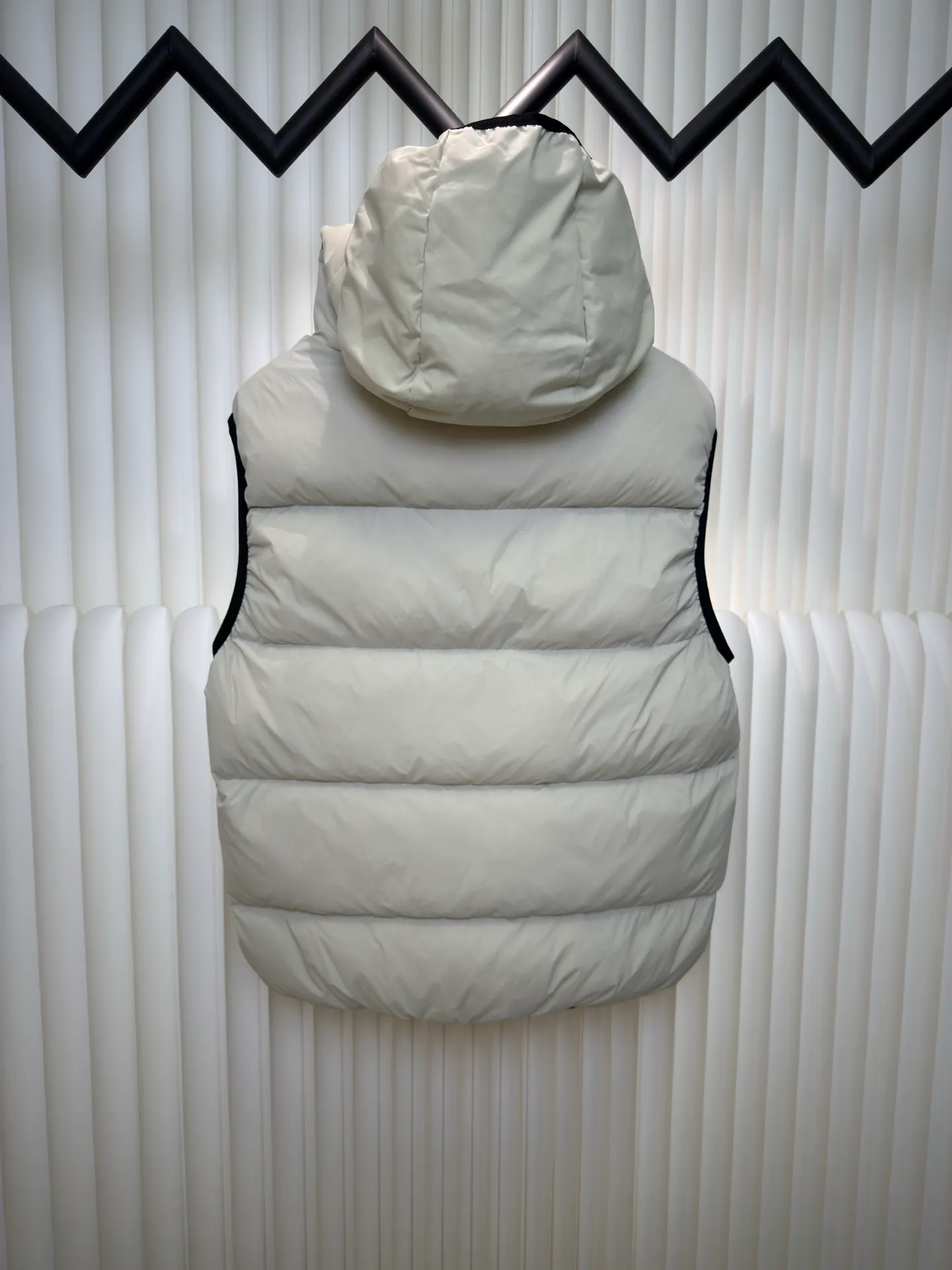 P660 MONCLER Badge Hooded Down Vest is made of nylon fabric made of 100% nylon. It is woven into a tight and tough fabric through advanced textile technology. It improves the strength of the frame and effectively blocks the invasion of cold wind and locks in the warm air generated by the down layer. After tight weaving and special treatment, it is waterproof and windproof. The surface forms a certain lotus leaf effect. It is also wrinkle-resistant and not easy to deform, making it easy for daily care.  The quilting stitches are sewn in a diagonal direction at an angle of about 70 degrees, and the diagonal lines are arranged in parallel. The fabric and filling are planned into different functional areas, and the quilting stitches in each partition are relatively independent. This allows the finished product to produce a larger deformation space along the diagonal direction when stretched and pressed, making it less likely to tighten and break, and has rich visual effects, modern and advanced features.  After the hood is removed, the stand-up collar displays an embossed logo of the same color, adding a unique visual experience and tactile details. High-quality filling: It is filled with 90% selected white duck down, weighing 170g, ensuring fluffy rebound, lightness and warmth. Size 1 2 3 4