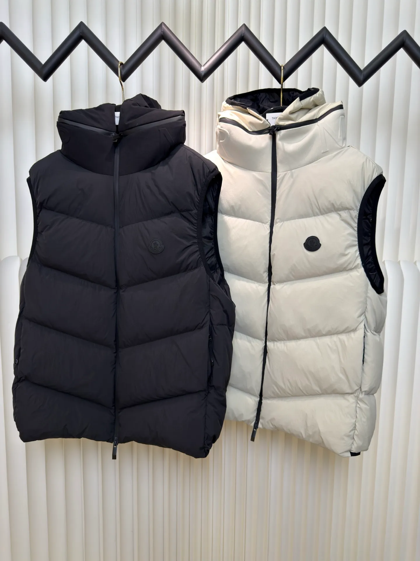 P660 MONCLER Badge Hooded Down Vest is made of nylon fabric made of 100% nylon. It is woven into a tight and tough fabric through advanced textile technology. It improves the strength of the frame and effectively blocks the invasion of cold wind and locks in the warm air generated by the down layer. After tight weaving and special treatment, it is waterproof and windproof. The surface forms a certain lotus leaf effect. It is also wrinkle-resistant and not easy to deform, making it easy for daily care.  The quilting stitches are sewn in a diagonal direction at an angle of about 70 degrees, and the diagonal lines are arranged in parallel. The fabric and filling are planned into different functional areas, and the quilting stitches in each partition are relatively independent. This allows the finished product to produce a larger deformation space along the diagonal direction when stretched and pressed, making it less likely to tighten and break, and has rich visual effects, modern and advanced features.  After the hood is removed, the stand-up collar displays an embossed logo of the same color, adding a unique visual experience and tactile details. High-quality filling: It is filled with 90% selected white duck down, weighing 170g, ensuring fluffy rebound, lightness and warmth. Size 1 2 3 4