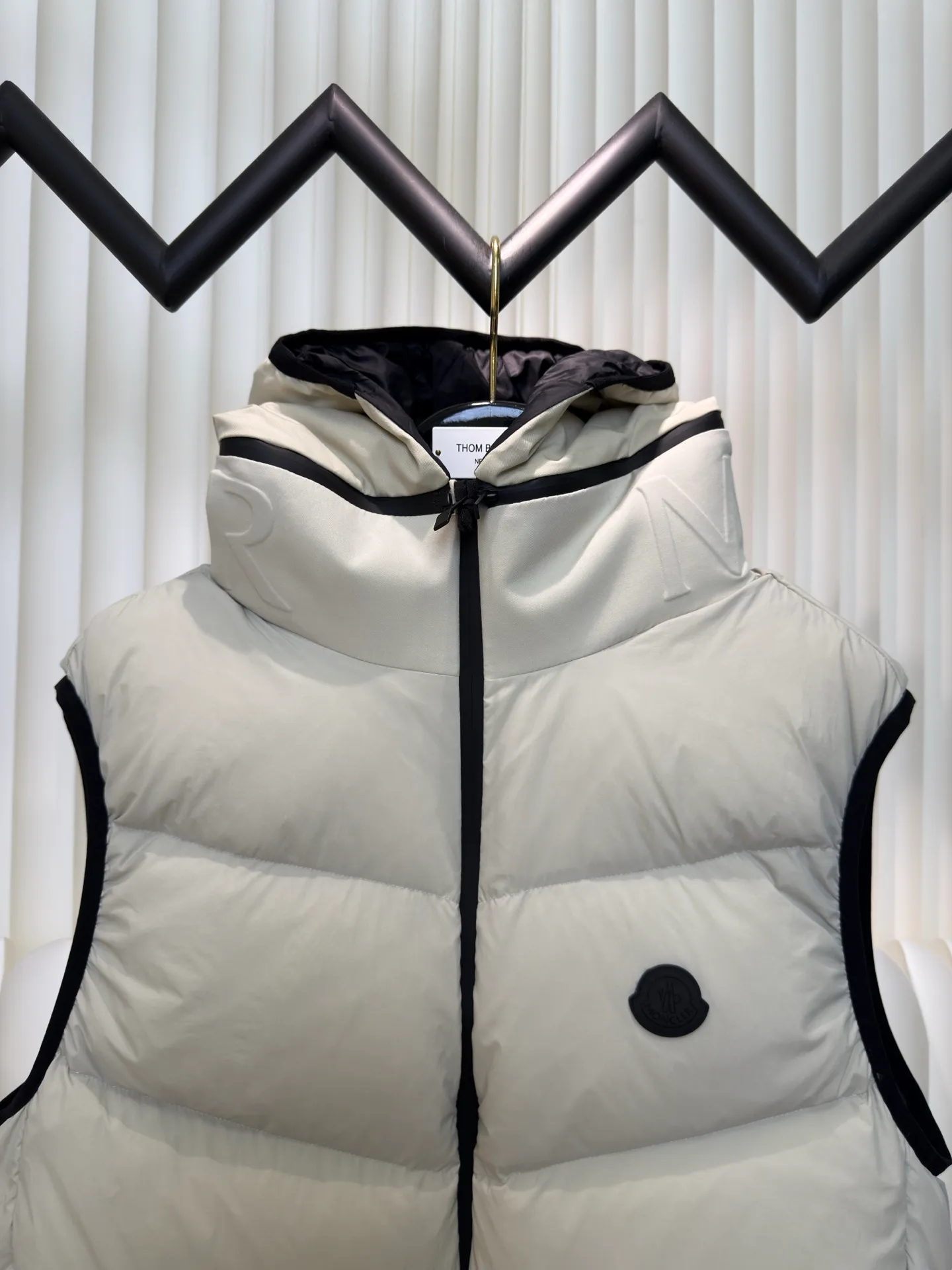 P660 MONCLER Badge Hooded Down Vest is made of nylon fabric made of 100% nylon. It is woven into a tight and tough fabric through advanced textile technology. It improves the strength of the frame and effectively blocks the invasion of cold wind and locks in the warm air generated by the down layer. After tight weaving and special treatment, it is waterproof and windproof. The surface forms a certain lotus leaf effect. It is also wrinkle-resistant and not easy to deform, making it easy for daily care.  The quilting stitches are sewn in a diagonal direction at an angle of about 70 degrees, and the diagonal lines are arranged in parallel. The fabric and filling are planned into different functional areas, and the quilting stitches in each partition are relatively independent. This allows the finished product to produce a larger deformation space along the diagonal direction when stretched and pressed, making it less likely to tighten and break, and has rich visual effects, modern and advanced features.  After the hood is removed, the stand-up collar displays an embossed logo of the same color, adding a unique visual experience and tactile details. High-quality filling: It is filled with 90% selected white duck down, weighing 170g, ensuring fluffy rebound, lightness and warmth. Size 1 2 3 4