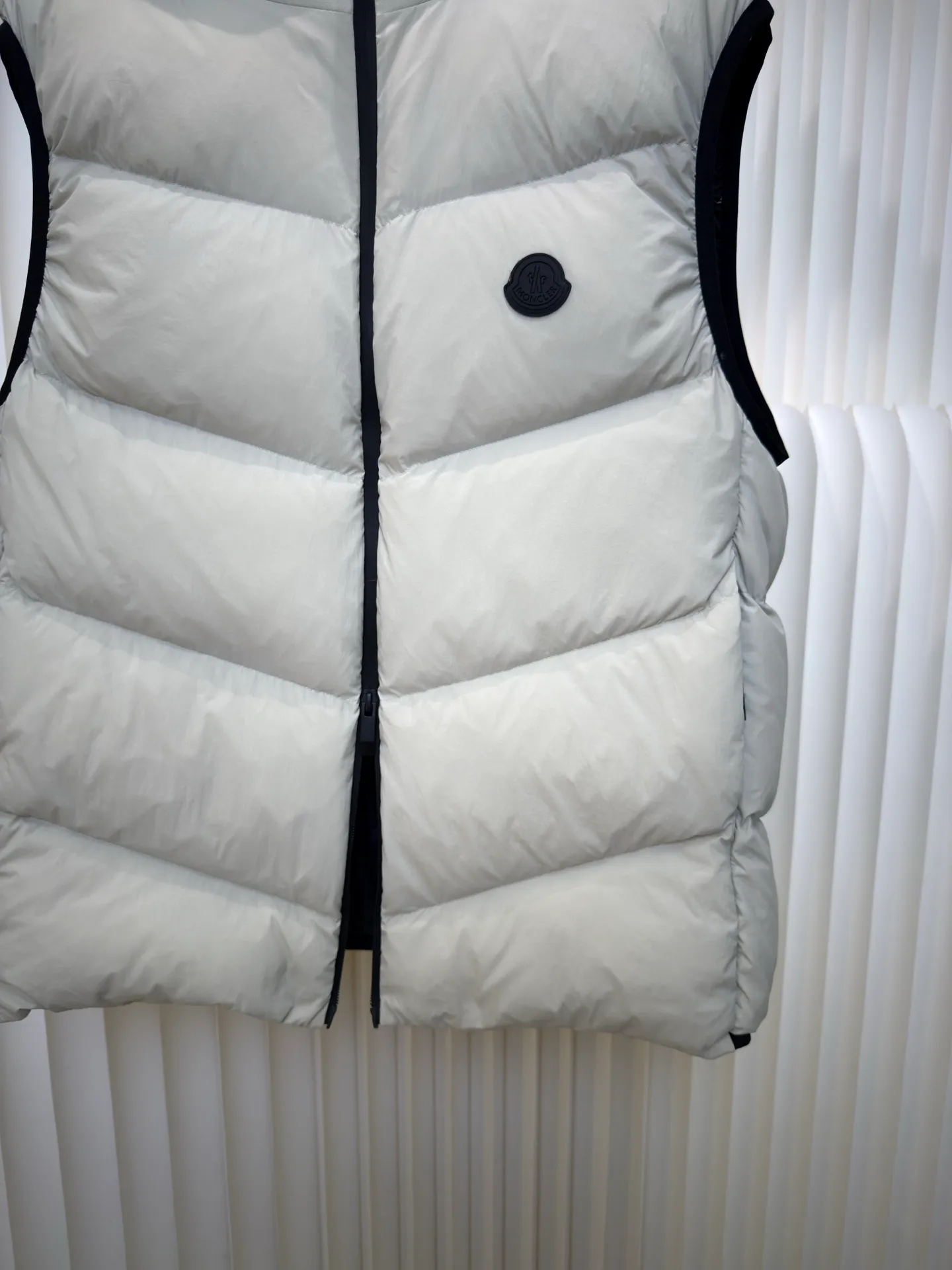 P660 MONCLER Badge Hooded Down Vest is made of nylon fabric made of 100% nylon. It is woven into a tight and tough fabric through advanced textile technology. It improves the strength of the frame and effectively blocks the invasion of cold wind and locks in the warm air generated by the down layer. After tight weaving and special treatment, it is waterproof and windproof. The surface forms a certain lotus leaf effect. It is also wrinkle-resistant and not easy to deform, making it easy for daily care.  The quilting stitches are sewn in a diagonal direction at an angle of about 70 degrees, and the diagonal lines are arranged in parallel. The fabric and filling are planned into different functional areas, and the quilting stitches in each partition are relatively independent. This allows the finished product to produce a larger deformation space along the diagonal direction when stretched and pressed, making it less likely to tighten and break, and has rich visual effects, modern and advanced features.  After the hood is removed, the stand-up collar displays an embossed logo of the same color, adding a unique visual experience and tactile details. High-quality filling: It is filled with 90% selected white duck down, weighing 170g, ensuring fluffy rebound, lightness and warmth. Size 1 2 3 4