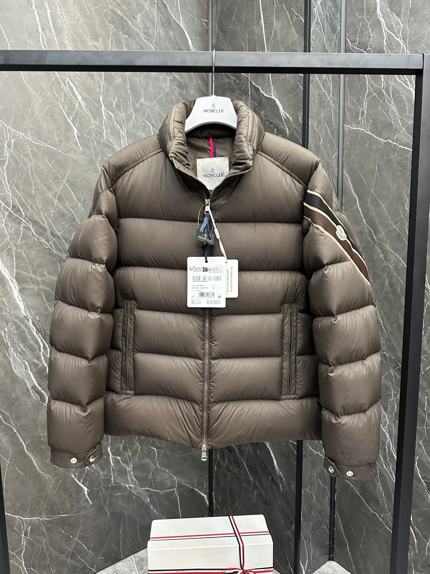 P920 2024N haute couture down moncler solayan men's three-color trimmed short down. Premium goose down filling. The most delicate, lightest and neatest fabric. Solayan men's short down is decorated with seasonal iconic stripe details, blending sportsmanship and timeless style. Solayan down is made of micro chic fabric and has a tough square shape design, highlighting Moncler's sporty spirit. This cropped style has tricolor stripes on the sleeves, a seasonal take on the brand's signature. Comes with a practical pull-out hood. Details · Made of micro chic nylon fabric · Micro chic nylon lining · Filled down · Pull-out hood · Zipper closure · Zipper pocket · Adjustable cuffs · Elastic drawstring hem · Tri-color trim on sleeves size: 1-5 Color: white, dark brown, black