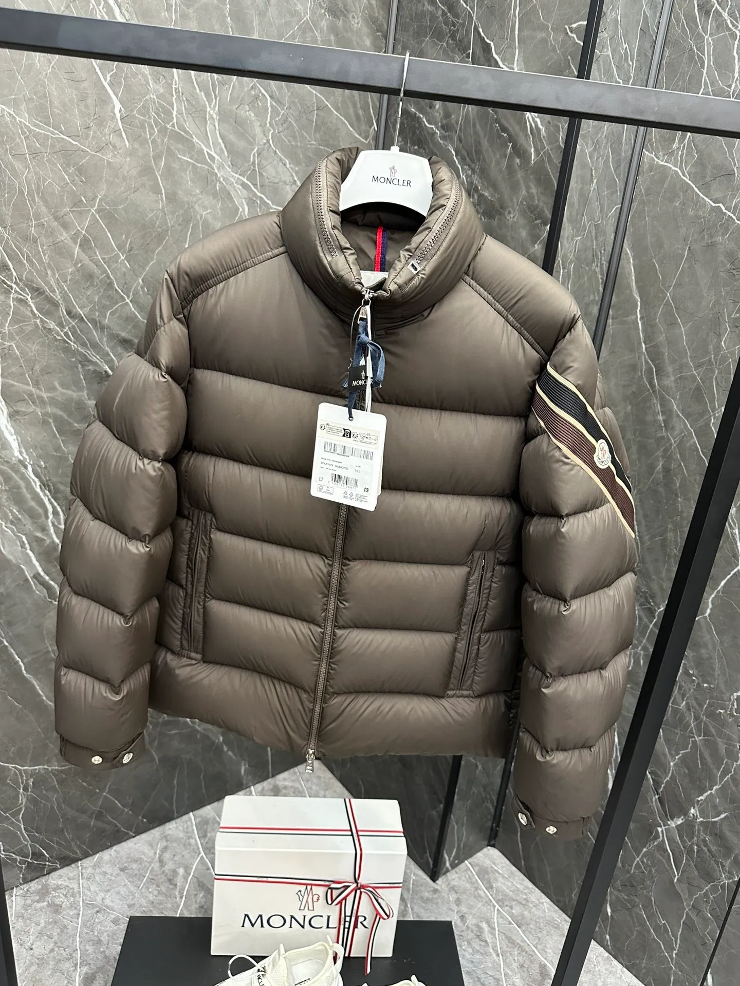 P920 2024N haute couture down moncler solayan men's three-color trimmed short down. Premium goose down filling. The most delicate, lightest and neatest fabric. Solayan men's short down is decorated with seasonal iconic stripe details, blending sportsmanship and timeless style. Solayan down is made of micro chic fabric and has a tough square shape design, highlighting Moncler's sporty spirit. This cropped style has tricolor stripes on the sleeves, a seasonal take on the brand's signature. Comes with a practical pull-out hood. Details · Made of micro chic nylon fabric · Micro chic nylon lining · Filled down · Pull-out hood · Zipper closure · Zipper pocket · Adjustable cuffs · Elastic drawstring hem · Tri-color trim on sleeves size: 1-5 Color: white, dark brown, black