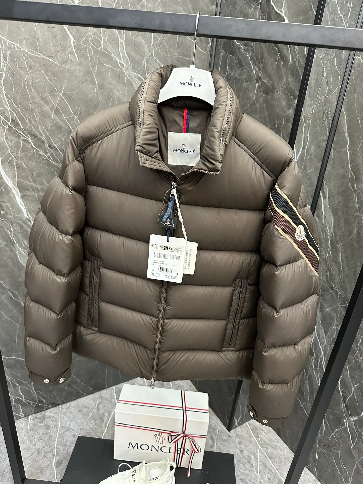 P920 2024N haute couture down moncler solayan men's three-color trimmed short down. Premium goose down filling. The most delicate, lightest and neatest fabric. Solayan men's short down is decorated with seasonal iconic stripe details, blending sportsmanship and timeless style. Solayan down is made of micro chic fabric and has a tough square shape design, highlighting Moncler's sporty spirit. This cropped style has tricolor stripes on the sleeves, a seasonal take on the brand's signature. Comes with a practical pull-out hood. Details · Made of micro chic nylon fabric · Micro chic nylon lining · Filled down · Pull-out hood · Zipper closure · Zipper pocket · Adjustable cuffs · Elastic drawstring hem · Tri-color trim on sleeves size: 1-5 Color: white, dark brown, black