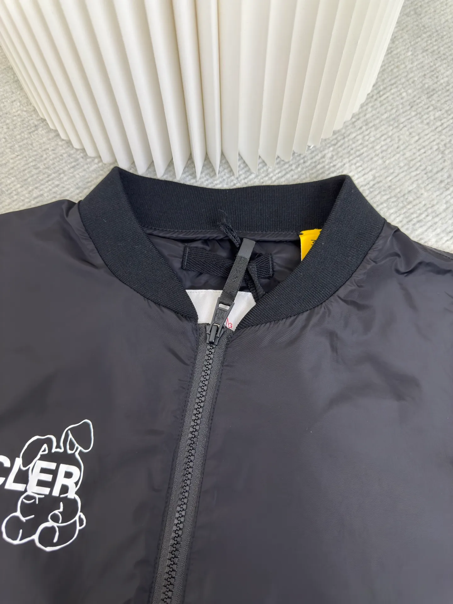 P530 Moncler Hiroshi Fujiwara co-branded bomber jacket is a coated nylon canvas fabric formed after nylon base material and coating treatment. The coating can effectively block moisture penetration, making it very waterproof. The nylon itself has high wear resistance. The ribbed knitted cotton collar and the cool luster of the coated nylon form a visual and physical contrast. The cotton ribbing is warm and skin-friendly, durable and not easily deformed after being washed. The zipper opens and closes, and a strap is attached to the zipper head to make it easier to open and close clothing. There are patch pockets on the left and right sides, and the edges of the pockets are reinforced with double-needle sewing technology, which is strong and beautiful at the same time. The cuffs and hem are closed with flat ribs to ensure no binding, ensuring wind resistance and warmth, and not easily deformed.  Screen glue printing. During the printing process of glue printing, the glue will form a thick colloid layer, making the printed pattern have a three-dimensional effect. It not only enhances the visual effect of printing, but also makes the hand feel richer. After the glue printing is cured, the printed pattern is closely integrated with the fabric and is not easy to fall off or wear. Size: 1 2 3 4