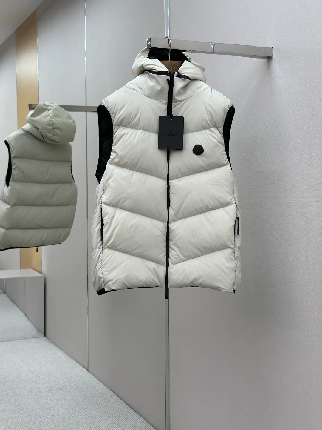 P660 MONCLER Badge Hooded Down Vest Fabric selection: Made of nylon fabric made of 100% nylon, which is woven into a tight and tough fabric through advanced textile technology. It improves the strength of the skeleton to effectively block the invasion of cold wind and lock the warm air generated by the down layer. After tight weaving and special treatment, it has waterproof and windproof functions. The surface forms a certain lotus leaf effect, and is wrinkle-resistant and not easily deformed, making it easy for daily care.  Technology: The quilting stitches are sewn in a diagonal direction at an angle of approximately 70 degrees. The diagonal lines are arranged in parallel. The fabric and filling are planned into different functional areas, and the quilting stitches in each partition are relatively independent. This allows the finished product to produce a larger deformation space along the diagonal direction when stretched and pressed, making it less likely to tighten and break, and has rich visual effects, modern and advanced features.  Details: After the hood is removed, the stand-up collar displays an embossed logo of the same color, adding a unique visual experience and tactile details.  High-quality filling: It is filled with 90% selected white duck down, weighing 170g, ensuring fluffy rebound, lightness and warmth.  Accessories: One-to-one customized zipper pendant, one-to-one customized badge, one-to-one customized three-label SIZE: 1 2 3 4