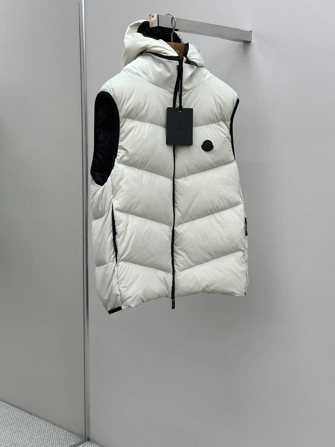 P660 MONCLER Badge Hooded Down Vest Fabric selection: Made of nylon fabric made of 100% nylon, which is woven into a tight and tough fabric through advanced textile technology. It improves the strength of the skeleton to effectively block the invasion of cold wind and lock the warm air generated by the down layer. After tight weaving and special treatment, it has waterproof and windproof functions. The surface forms a certain lotus leaf effect, and is wrinkle-resistant and not easily deformed, making it easy for daily care.  Technology: The quilting stitches are sewn in a diagonal direction at an angle of approximately 70 degrees. The diagonal lines are arranged in parallel. The fabric and filling are planned into different functional areas, and the quilting stitches in each partition are relatively independent. This allows the finished product to produce a larger deformation space along the diagonal direction when stretched and pressed, making it less likely to tighten and break, and has rich visual effects, modern and advanced features.  Details: After the hood is removed, the stand-up collar displays an embossed logo of the same color, adding a unique visual experience and tactile details.  High-quality filling: It is filled with 90% selected white duck down, weighing 170g, ensuring fluffy rebound, lightness and warmth.  Accessories: One-to-one customized zipper pendant, one-to-one customized badge, one-to-one customized three-label SIZE: 1 2 3 4