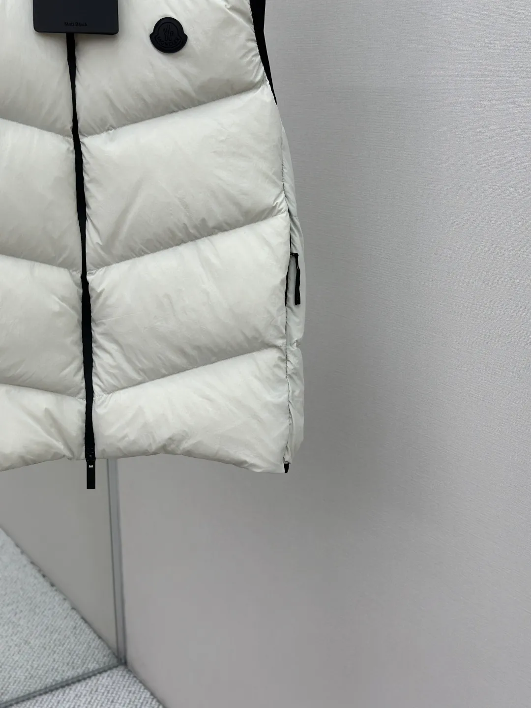 P660 MONCLER Badge Hooded Down Vest Fabric selection: Made of nylon fabric made of 100% nylon, which is woven into a tight and tough fabric through advanced textile technology. It improves the strength of the skeleton to effectively block the invasion of cold wind and lock the warm air generated by the down layer. After tight weaving and special treatment, it has waterproof and windproof functions. The surface forms a certain lotus leaf effect, and is wrinkle-resistant and not easily deformed, making it easy for daily care.  Technology: The quilting stitches are sewn in a diagonal direction at an angle of approximately 70 degrees. The diagonal lines are arranged in parallel. The fabric and filling are planned into different functional areas, and the quilting stitches in each partition are relatively independent. This allows the finished product to produce a larger deformation space along the diagonal direction when stretched and pressed, making it less likely to tighten and break, and has rich visual effects, modern and advanced features.  Details: After the hood is removed, the stand-up collar displays an embossed logo of the same color, adding a unique visual experience and tactile details.  High-quality filling: It is filled with 90% selected white duck down, weighing 170g, ensuring fluffy rebound, lightness and warmth.  Accessories: One-to-one customized zipper pendant, one-to-one customized badge, one-to-one customized three-label SIZE: 1 2 3 4