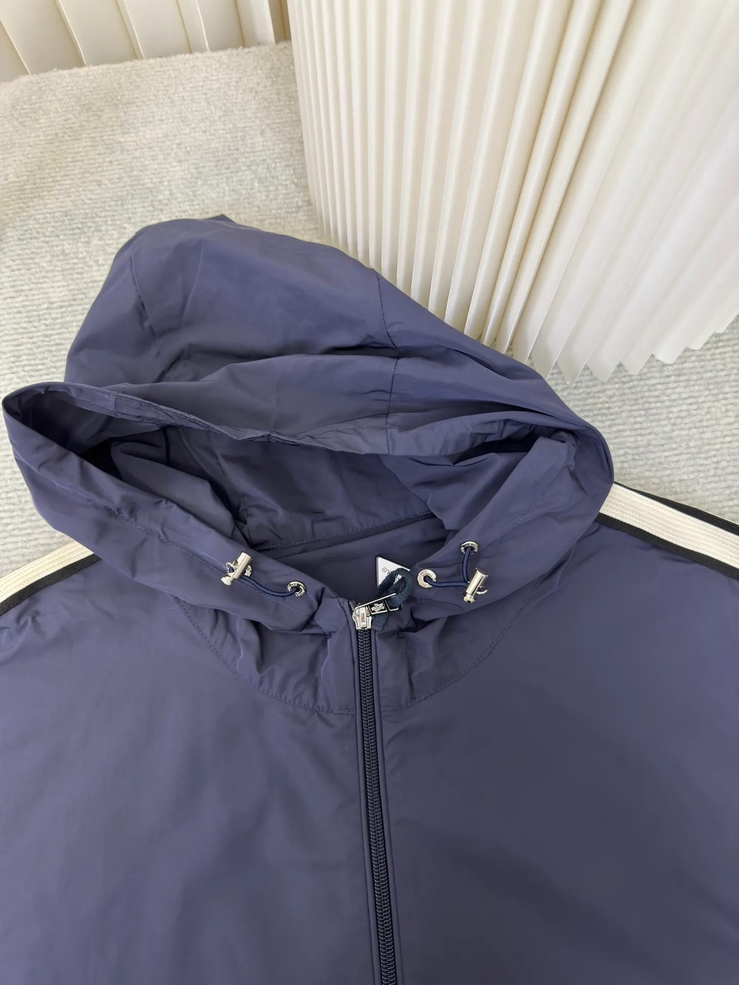 P570 MONCLER lightweight jacket with web trim at the mouth is made of 100% polyester fiber to create a tough protective outer layer. It is famous for its excellent tear resistance and wear resistance. It can quickly return to flatness during wearing and maintain the crisp and stylish appearance of the clothing for a long time. At the same time, it is not easy to deform after being washed for a long time.  Decorative edging in two different colors has been added to the center section of the sleeves. This design element not only adds visual highlights to clothing, making it more fashionable and unique. The webbing is precisely positioned along the cuffs to the seam of the collar and hat to ensure symmetry and overall smoothness. Before actual sewing, use very fine basting stitches for pre-fixing. This step is crucial to prevent the webbing from slipping, twisting, or wrinkling during sewing and ensuring that the final stitch is straight and perfect. Size 1 2 3 4