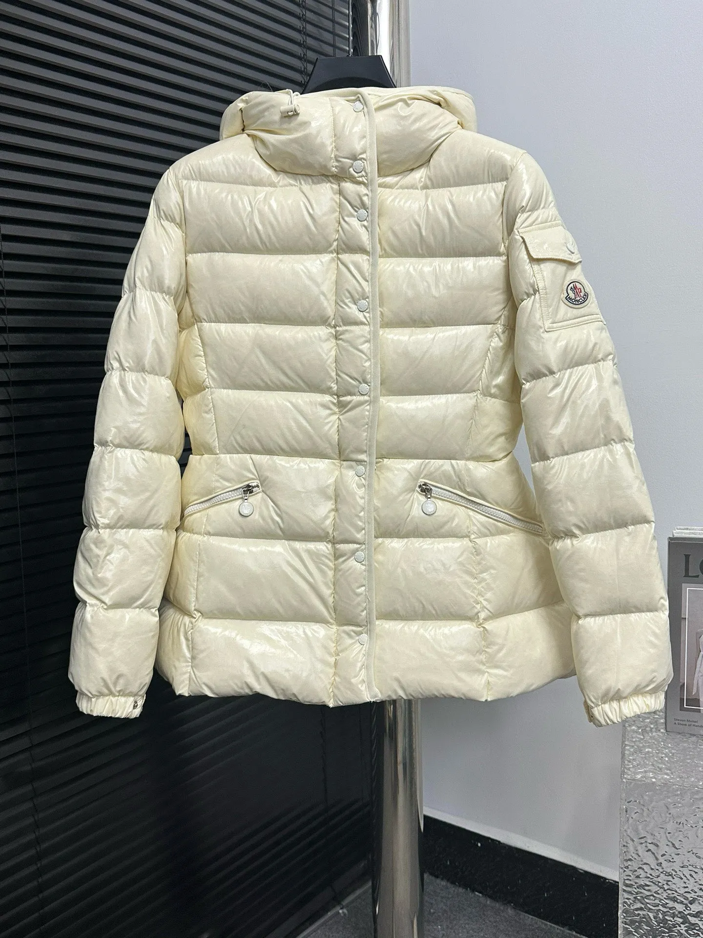 P860 [Moncler] Hooded, waisted women's short down jacket. The barante down jacket is made of glossy nylon fabric and is inspired by the 1970s. It adopts a waist design and presents an A-line silhouette, highlighting a feminine style. An adjustable hood and signature logo patch add finishing touches. Details · Made of lon laqué fabric · lon laqué lining · Filled with down · Adjustable hood · Zipper and snap closure · Suit pocket · Adjustable cuffs Size: 0/1/2/3