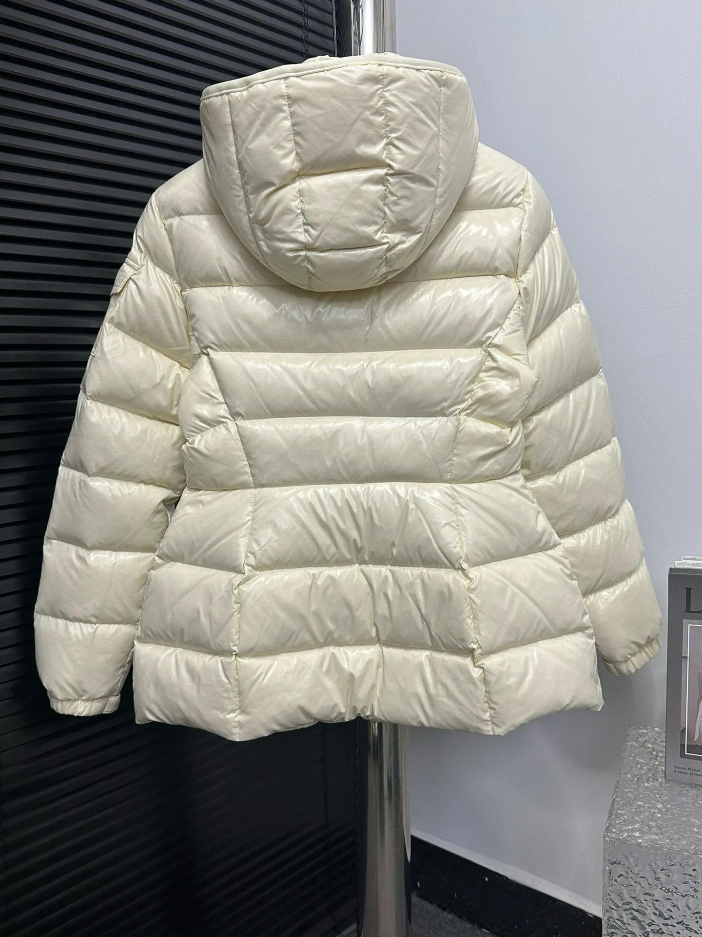 P860 [Moncler] Hooded, waisted women's short down jacket. The barante down jacket is made of glossy nylon fabric and is inspired by the 1970s. It adopts a waist design and presents an A-line silhouette, highlighting a feminine style. An adjustable hood and signature logo patch add finishing touches. Details · Made of lon laqué fabric · lon laqué lining · Filled with down · Adjustable hood · Zipper and snap closure · Suit pocket · Adjustable cuffs Size: 0/1/2/3