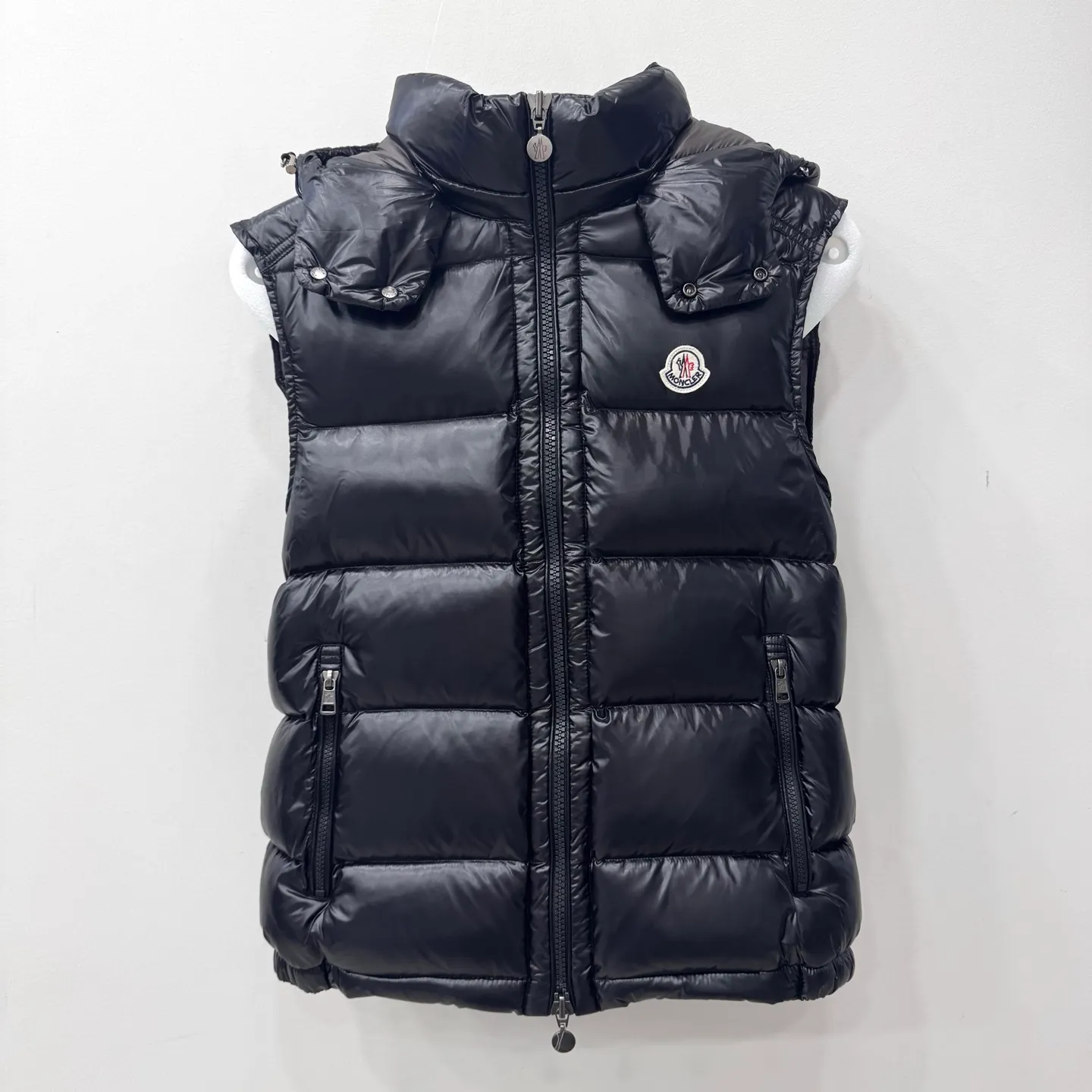 P580 Bormes Men's Hooded Down Vest] The Bormes men's vest is classic and timeless, with colors and details reminiscent of the Paninari trend of the 1980s.    The Bormes down vest is made from signature glossy nylon laqué fabric with classic checkered quilting for excellent warmth and protection. Two-way zipper closure design, with Moncler logo-shaped zipper puller.  • Made of nylon laqué • Nylon laqué lining • Filled with down • Detachable and adjustable hood • Collar with press buttons • Zipper closure • Zippered pockets • Fabric: 100% nylon; • Lining: 100% nylon; • Filling: Goose down • Down content: 90%; excluding upholstery; • Size: 12345 Maximum wash temperature 30°C - Gentle wash; Do not bleach; Do not tumble dry; Iron maximum temperature 110°C - without steam; Do not dry clean; Professional wet cleaning - gentle wash; Lay flat to dry in shade; Wash separately; Recommend washing and ironing inside out