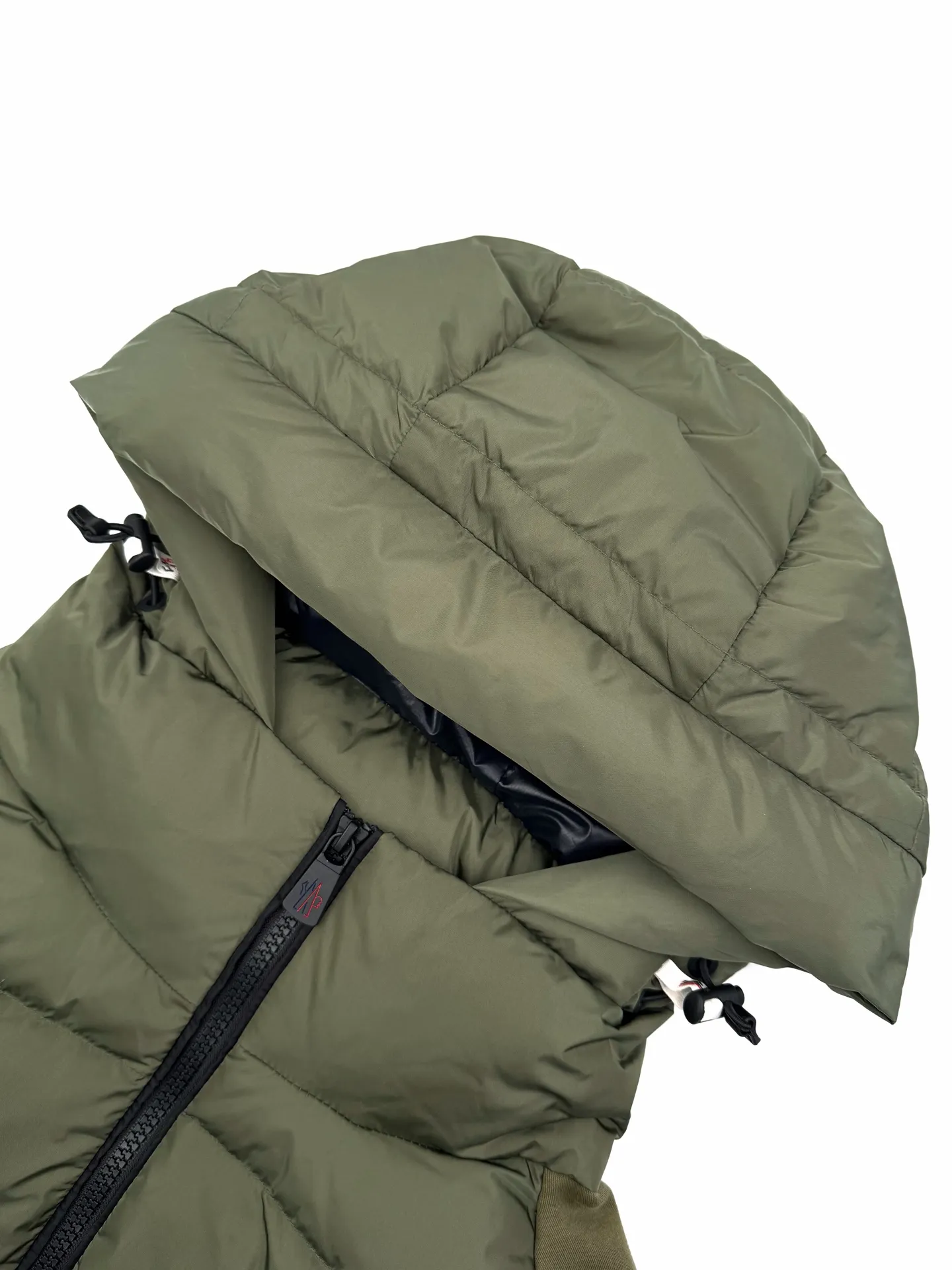 P780 Moncler logo woven splicing down jacket, custom-made matte lattice air shield down and 300D high-density calendered coating, using the new national standard 90 white duck down (welcome to test), full of down, full of warmth, light and fluffy, with the dark green of the overlapping mountains as the background, all things accumulating, creating its own scenery in silence The Monlcer triangle logo is embellished on the chest, the power aesthetics of the minimalist logo The concentrated down filling in the front area creates dynamic insulation for the core heat dissipation zone of the human body. The hooded down is a moving warm flow barrier for the head and neck, forming a thermal energy circulation system with the front area. The elastic woven sleeves provide freedom of movement with a sense of compression, forming a relaxed and warm philosophy. The real high-end is to let function become the footnote of style. Process 1: Computer mechanical down filling. Prioritize the liner pattern by making a pattern to determine the down filling area and determine the weight of down per square meter according to the original three-dimensional effect. Thus, the amount of down filling for each cut piece is calculated. The computer down filling machine uses a digital weighing unit to achieve stable measurement. Process 2: 3D three-dimensional quilting technology. With the programming system of the CNC quilting machine, the down in different areas is accurately separated to ensure that the filling is evenly fixed after sewing and avoid agglomeration or displacement. Process 3: Computer template machine line running process. The computer template machine line line process shows extremely high neatness and smoothness. The craftsman's precise control of the size during the operation ensures that each line meets the design requirements. The lines of the entire template are smooth and unified, neat and beautiful. Process 4: Triple locking five-thread dense stitching process. Main seam locking + diagonal reinforcement + raw edge wrapping. Triple structure to form a three-dimensional protective net at the edge of the fabric to avoid stitch breakage. Paving materials: Customized 1:1 Moncler zipper. Customized 1:1 Moncler rope loop. Customized 1:1 Moncler logo. Customized 1:1 Moncler. Corns Customized 1:1 Moncler trademark Size: S M L XL Style number: 25378