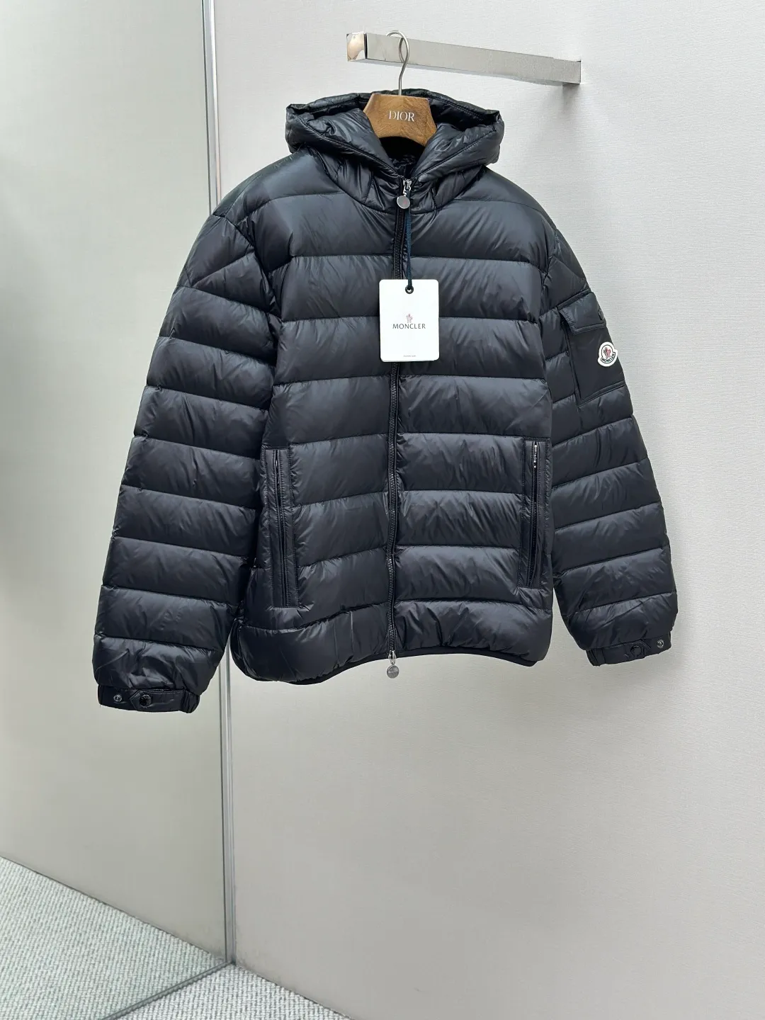 P910 MONCLER hooded brim quilted embroidered down jacket Fabric selection: The longue saison fabric is made of high-count polyamide fiber, which is known for its excellent tensile strength and lightness. Its good flexibility makes the fabric less prone to wrinkles and keeps it crisp and stylish for a long time. The tight weave effectively blocks the invasion of cold wind and locks in the warm air generated by the down layer. The high-density nylon surface forms a certain lotus leaf effect, making it difficult for small water droplets to penetrate, keeping the interior dry and effectively extending the service life of the down.  Lining selection: High-density lining fabric made of ultra-fine denier, 0.08mm thickness to avoid increasing the overall weight and making it smooth to wear. The high-density woven structure forms a wind resistance layer to protect the thermal efficiency of the thermal layer from loss. It can also withstand the expansion pressure of down and prevent deformation and damage after long-term use.  Technology: The quilted letter logo on the brim uses contour quilting technology. The stitching is routed along the edge of the set outline, and the filler is compressed inside the letter graphic, so that the logo is three-dimensional and convex, and the pattern is clear.  High-quality filling: It is filled with 90% selected white duck down, weighing 210g, ensuring fluffy rebound, lightness and warmth.  Accessories: customized zipper pendant, customized badge, customized three-label SIZE: 1 2 3 4