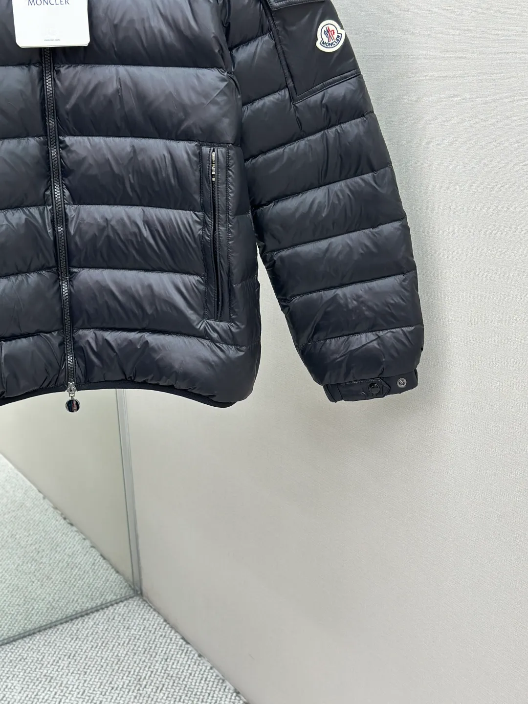 P910 MONCLER hooded brim quilted embroidered down jacket Fabric selection: The longue saison fabric is made of high-count polyamide fiber, which is known for its excellent tensile strength and lightness. Its good flexibility makes the fabric less prone to wrinkles and keeps it crisp and stylish for a long time. The tight weave effectively blocks the invasion of cold wind and locks in the warm air generated by the down layer. The high-density nylon surface forms a certain lotus leaf effect, making it difficult for small water droplets to penetrate, keeping the interior dry and effectively extending the service life of the down.  Lining selection: High-density lining fabric made of ultra-fine denier, 0.08mm thickness to avoid increasing the overall weight and making it smooth to wear. The high-density woven structure forms a wind resistance layer to protect the thermal efficiency of the thermal layer from loss. It can also withstand the expansion pressure of down and prevent deformation and damage after long-term use.  Technology: The quilted letter logo on the brim uses contour quilting technology. The stitching is routed along the edge of the set outline, and the filler is compressed inside the letter graphic, so that the logo is three-dimensional and convex, and the pattern is clear.  High-quality filling: It is filled with 90% selected white duck down, weighing 210g, ensuring fluffy rebound, lightness and warmth.  Accessories: customized zipper pendant, customized badge, customized three-label SIZE: 1 2 3 4