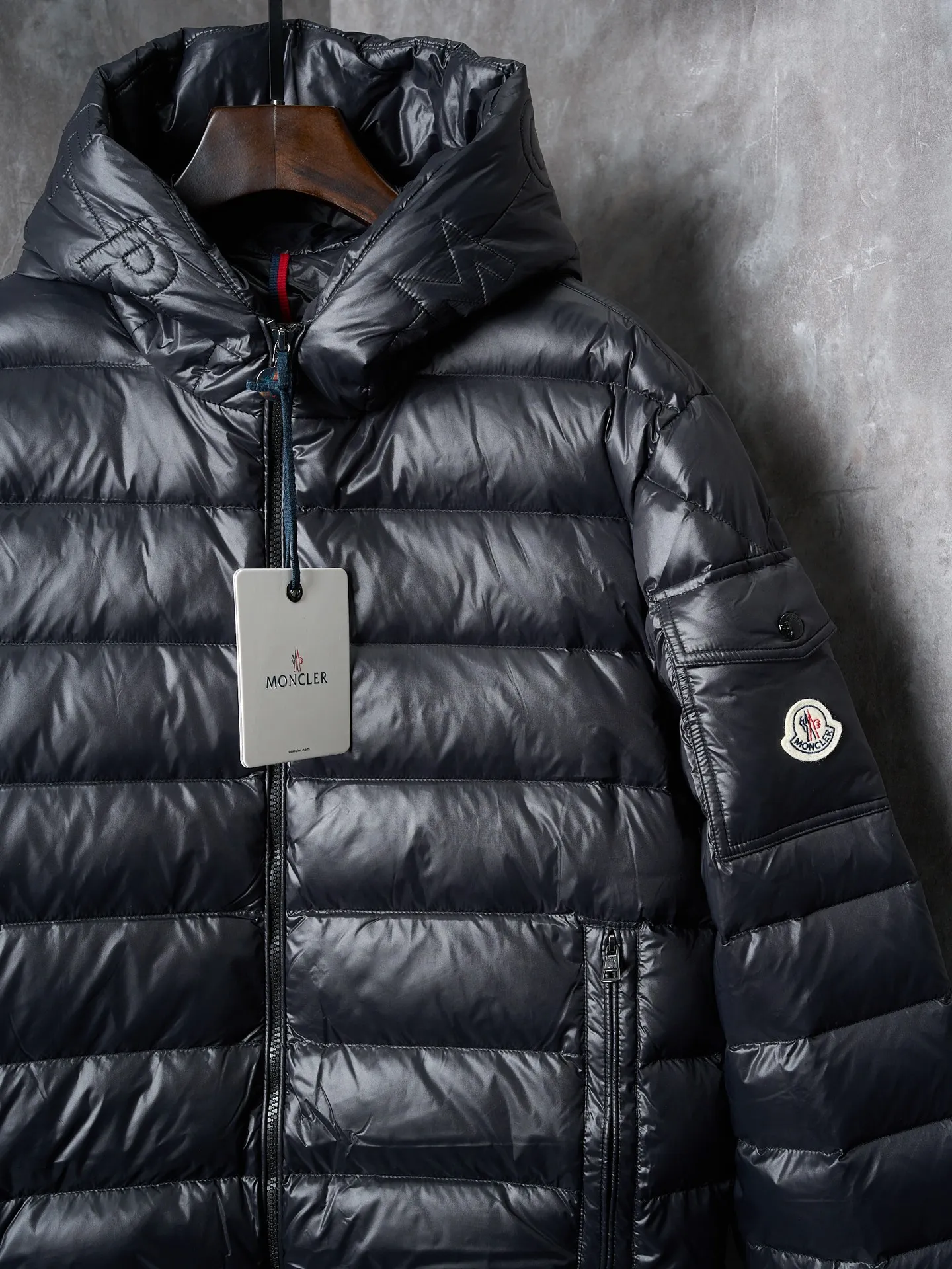 P900 Actual hanging auction] MONCLER/Maskled brim quilted embroidered pocket logo hooded down jacket [Ready stock] 1 2 3 4 Filled with 90 selected white duck down, weighing 210g, ensuring fast fluffy rebound, lightness and warmth.  The longue saison fabric made of high-count polyamide fiber is famous for its excellent tensile strength and lightness. Its good flexibility makes the fabric less prone to wrinkles and keeps it crisp and stylish for a long time. The tight weave effectively blocks the invasion of cold wind and locks in the warm air generated by the down layer. The high-density nylon surface forms a certain lotus leaf effect, making it difficult for small water droplets to penetrate, keeping the interior dry and effectively extending the service life of the down.  The high-density lining is woven with ultra-fine denier, with a thickness of 0.08mm to avoid increasing the overall weight and making it smooth to wear. The high-density woven structure forms a wind resistance layer to protect the thermal efficiency of the thermal layer from loss. It can also withstand the expansion pressure of down and prevent deformation and damage after long-term use.  The quilted letter logo on the brim uses contour quilting technology. The stitches are routed along the edge of the set outline, and the filler is compressed inside the letter graphic, so that the logo is three-dimensional and the pattern is clear.