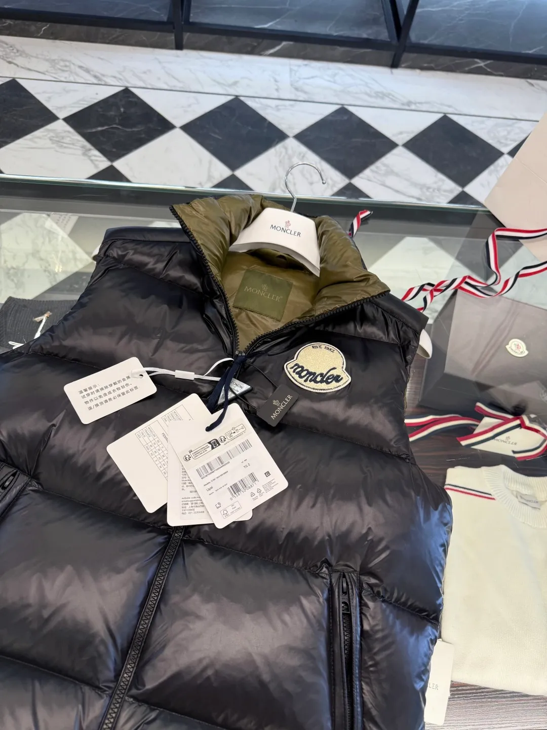 P660 Moncler Lipsi down vest. Contrast color splicing design. Super full filling. Lipsi men's down vest is made of shiny nylon laqué fabric, suitable for wearing in different seasons, bringing warmth and care.  The Lipsi short down vest embodies Moncler's classic design and is a must-have item for your wardrobe from season to season. Crafted from lightweight, functional nylon laqué fabric, it has a contrast lining for a vibrant feel. Details •Made from lightweight nylon laqué fabric •Lightweight nylon laqué lining •Filled with down •Stand-up collar •Zipper closure •Zip pockets •Chenille logo patch Size: 1-5 Black/Ivory Couple Style