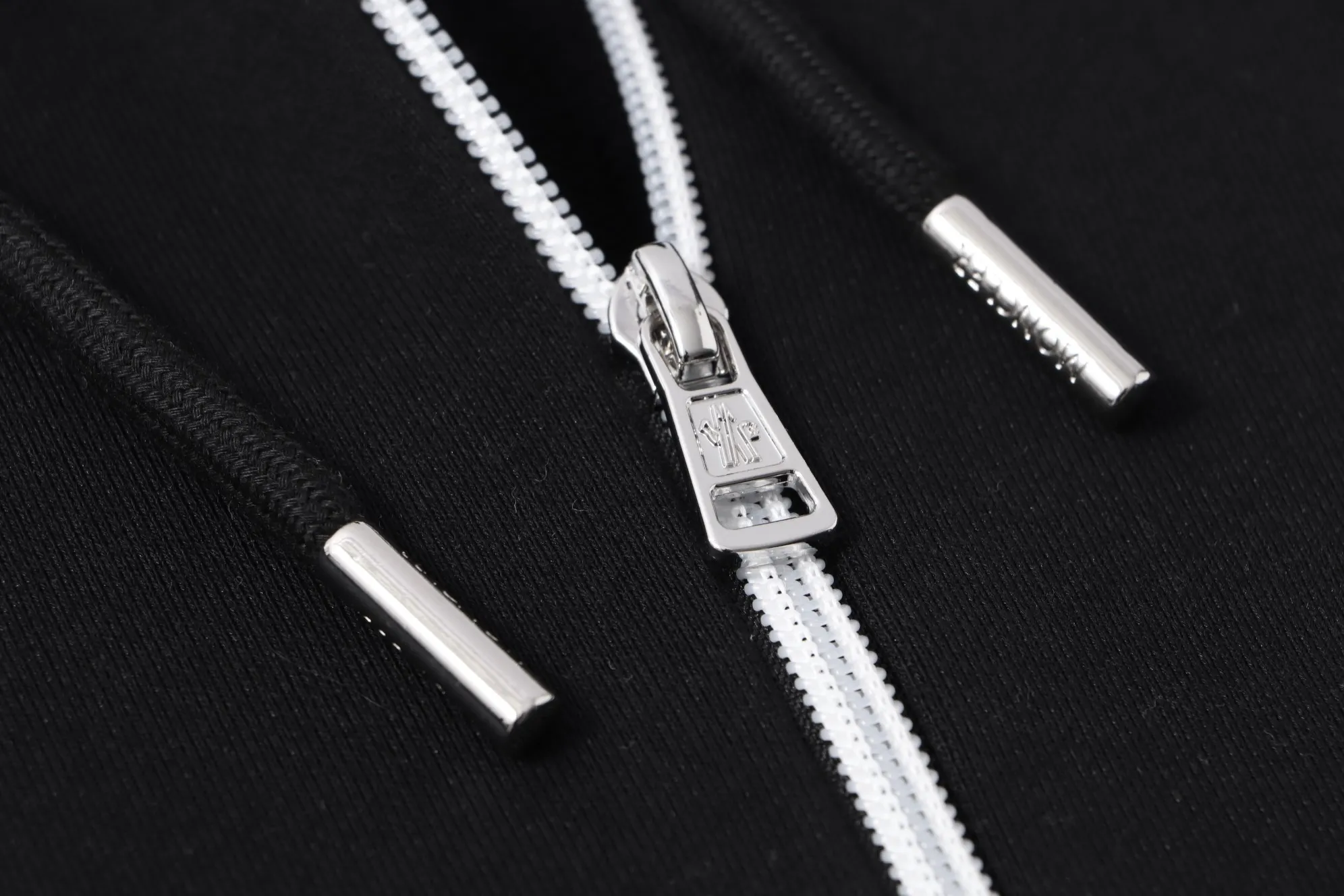 P340 💰 Moncler's new slogan printed zipper hooded jacket is made of lightweight turned velvet cotton fabric. High-density cotton fiber is used to achieve internal and external differentiation in a single layer of fabric. The outer plain weave is tight and wear-resistant, and the inner layer is formed into a short dense suede surface through a sanding process. The dense plain weave structure resists wind and splashes, the brushed suede surface is skin-friendly, and the short pile has been treated to eliminate static electricity to avoid sticking to the skin. A very small amount of grooved polyester moisture-conducting yarn is embedded in the cotton fiber, which quickly guides sweat from the inner suede surface to the outer layer for evaporation through the capillary effect, solving the problem of the suede being easily stuffy. By actively interfering with the shrinkage potential of cotton fibers, the fabric is able to transition from changeable to stable, improving dimensional stability while being less prone to deformation and wrinkles. High saturation is achieved on the center of the cap through glue printing. Size: xs-l
