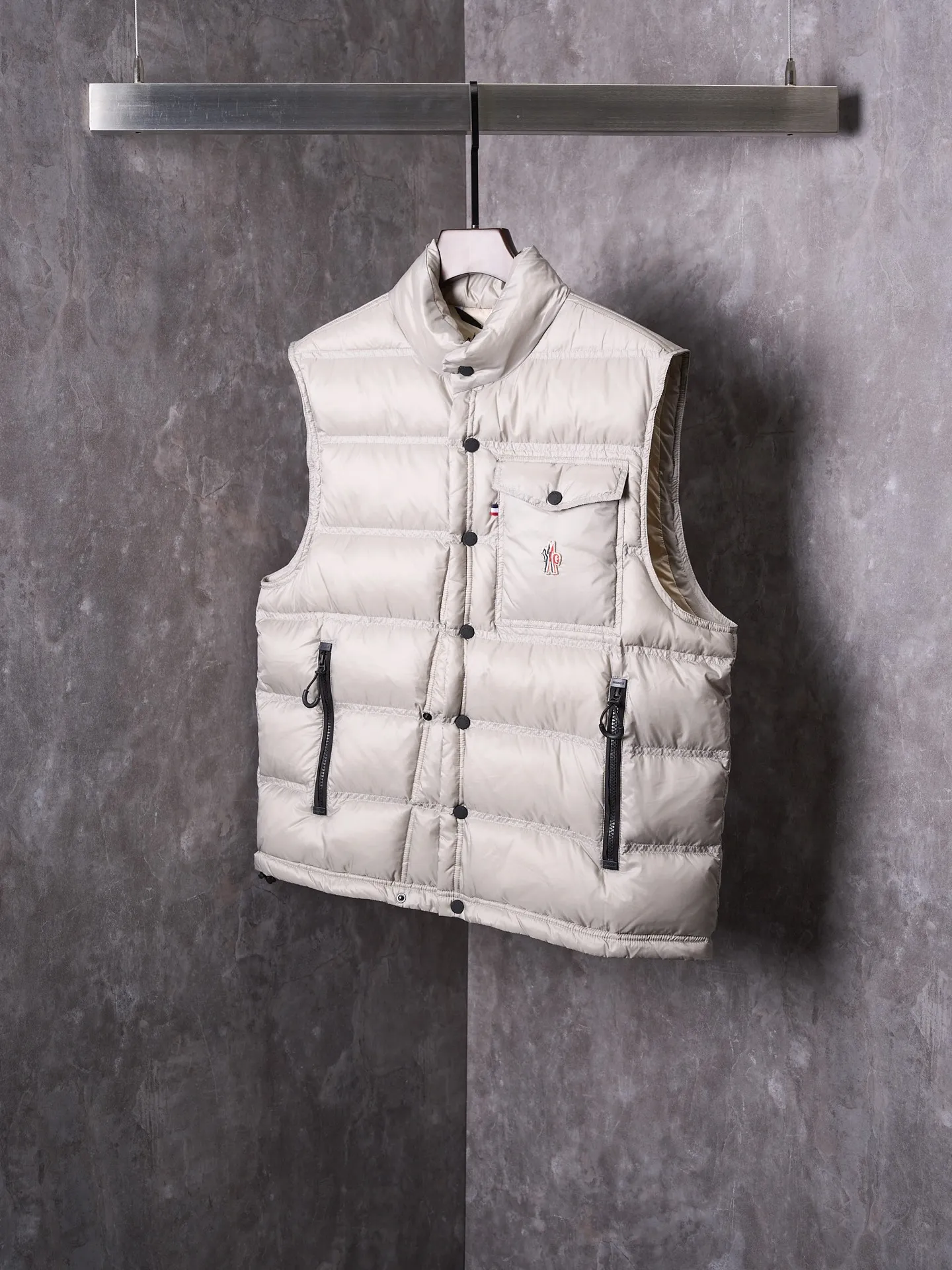 P680 Actual hanging auction] MONCLER/Mandow embroidered reflective logo stand-up collar down vest [Ready stock] 1 2 3 4 It is made of extremely fine nylon yarn and woven in a high-density way. The number of yarns per unit area is large, and the gaps between the yarns are very small, which can effectively block the penetration of cold wind. The fine weave keeps it lightweight and soft to the touch, physically restricting the lightweight down fibers from slipping through the gaps. Nylon fiber itself has good wear resistance and is not easy to snag, which significantly extends its service life and can easily cope with the needs of multiple scenarios.  The lining is made of high-density weaving of 100% polyester fiber, with a thickness of 0.08mm to avoid increasing the overall weight and making it smooth to wear. The high-density weaving structure forms a wind resistance layer to protect the thermal efficiency of the thermal layer from loss. It can withstand the expansion pressure of down and prevent deformation and damage after long-term use.  It uses 90 white duck down with a weight of 130g to ensure excellent thermal insulation performance. After strict screening and processing, the velvet is not easy to get drilled, ensuring durability.  Through the reflective cloth punching process, the logo is regularly arranged on the triangular reflective mark with dozens of small holes, which not only improves functionality but also enhances recognition and aesthetics.