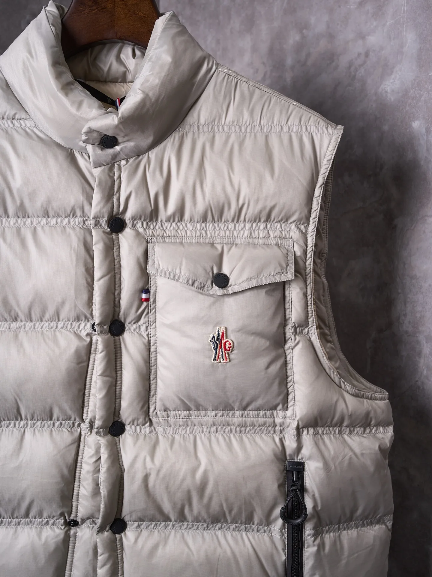 P680 Actual hanging auction] MONCLER/Mandow embroidered reflective logo stand-up collar down vest [Ready stock] 1 2 3 4 It is made of extremely fine nylon yarn and woven in a high-density way. The number of yarns per unit area is large, and the gaps between the yarns are very small, which can effectively block the penetration of cold wind. The fine weave keeps it lightweight and soft to the touch, physically restricting the lightweight down fibers from slipping through the gaps. Nylon fiber itself has good wear resistance and is not easy to snag, which significantly extends its service life and can easily cope with the needs of multiple scenarios.  The lining is made of high-density weaving of 100% polyester fiber, with a thickness of 0.08mm to avoid increasing the overall weight and making it smooth to wear. The high-density weaving structure forms a wind resistance layer to protect the thermal efficiency of the thermal layer from loss. It can withstand the expansion pressure of down and prevent deformation and damage after long-term use.  It uses 90 white duck down with a weight of 130g to ensure excellent thermal insulation performance. After strict screening and processing, the velvet is not easy to get drilled, ensuring durability.  Through the reflective cloth punching process, the logo is regularly arranged on the triangular reflective mark with dozens of small holes, which not only improves functionality but also enhances recognition and aesthetics.