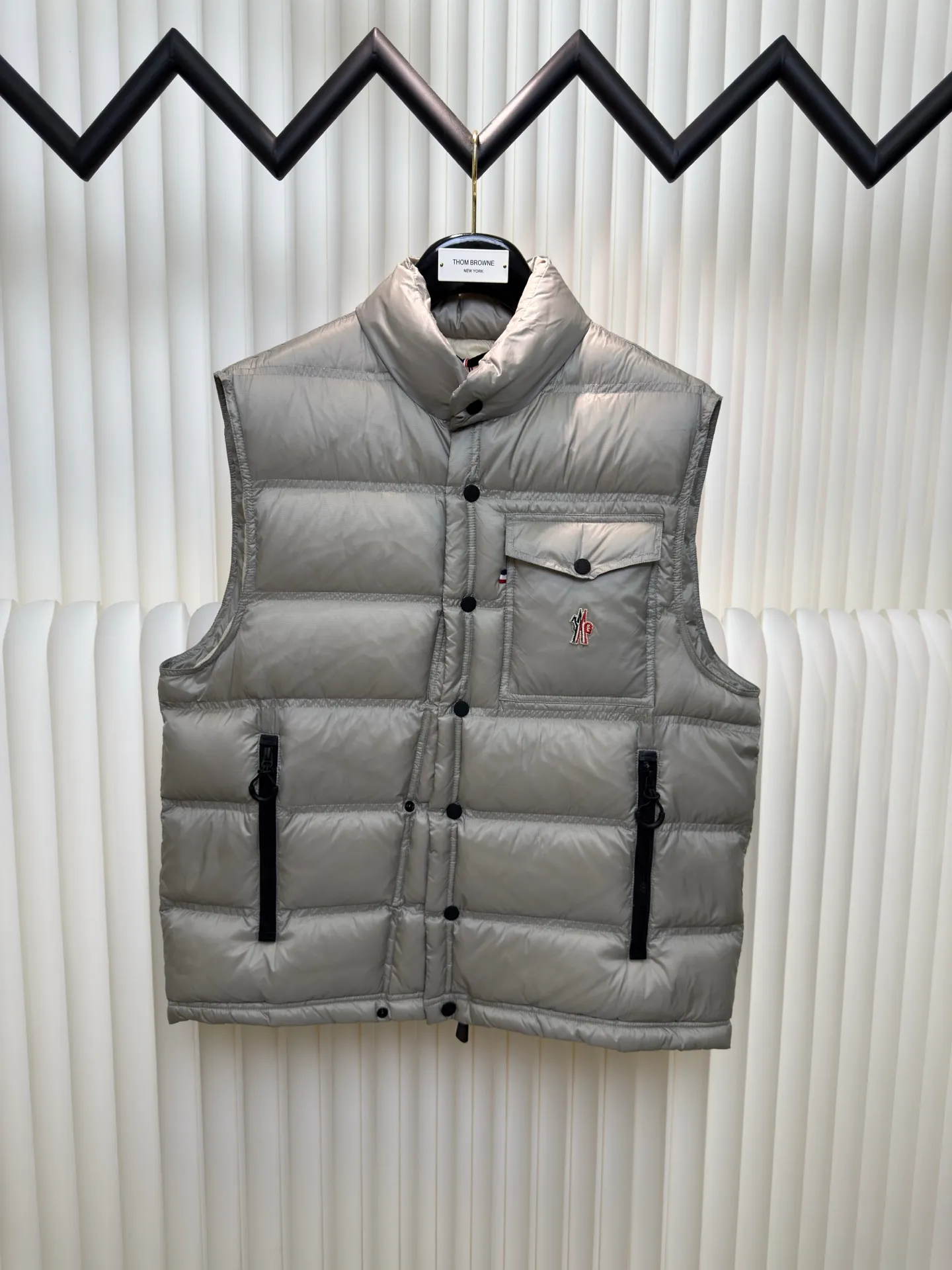 P700 MONCLER masked down vest with reflective markings is made of 90 white duck down with a weight of 130g to ensure excellent thermal insulation performance. After strict screening and processing, the velvet is not easy to get drilled, ensuring durability.  It is made of extremely fine nylon yarn and is woven in a high-density manner. The number of yarns per unit area is large, and the gaps between the yarns are very small, which can effectively block the penetration of cold wind. The fine weave keeps it lightweight and soft to the touch, physically restricting the lightweight down fibers from slipping through the gaps. Nylon fiber itself has good wear resistance and is not easy to snag, which significantly extends its service life and can easily cope with the needs of multiple scenarios.  The lining is made of high-density weaving of 100% polyester fiber, with a thickness of 0.08mm to avoid increasing the overall weight and making it smooth to wear. The high-density weaving structure forms a wind resistance layer to protect the thermal efficiency of the thermal layer from loss. It can withstand the expansion pressure of down and prevent deformation and damage after long-term use.  Through the reflective cloth punching process, the logo is regularly arranged on the triangular reflective mark with dozens of small holes, which not only improves functionality but also enhances recognition and aesthetics. Size 1 2 3 4