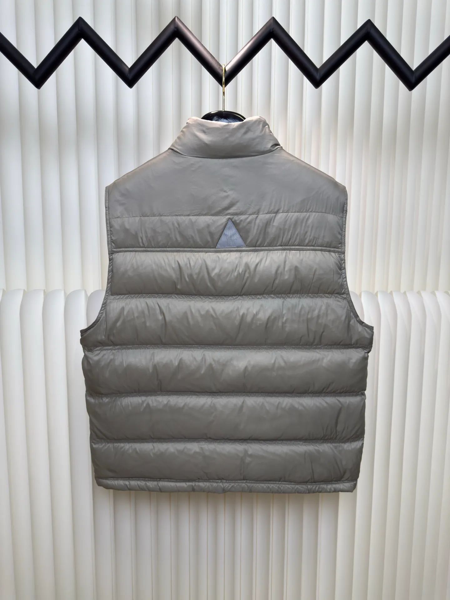 P700 MONCLER masked down vest with reflective markings is made of 90 white duck down with a weight of 130g to ensure excellent thermal insulation performance. After strict screening and processing, the velvet is not easy to get drilled, ensuring durability.  It is made of extremely fine nylon yarn and is woven in a high-density manner. The number of yarns per unit area is large, and the gaps between the yarns are very small, which can effectively block the penetration of cold wind. The fine weave keeps it lightweight and soft to the touch, physically restricting the lightweight down fibers from slipping through the gaps. Nylon fiber itself has good wear resistance and is not easy to snag, which significantly extends its service life and can easily cope with the needs of multiple scenarios.  The lining is made of high-density weaving of 100% polyester fiber, with a thickness of 0.08mm to avoid increasing the overall weight and making it smooth to wear. The high-density weaving structure forms a wind resistance layer to protect the thermal efficiency of the thermal layer from loss. It can withstand the expansion pressure of down and prevent deformation and damage after long-term use.  Through the reflective cloth punching process, the logo is regularly arranged on the triangular reflective mark with dozens of small holes, which not only improves functionality but also enhances recognition and aesthetics. Size 1 2 3 4