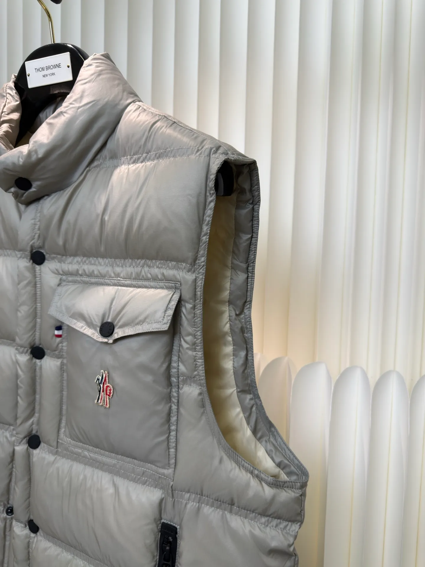 P700 MONCLER masked down vest with reflective markings is made of 90 white duck down with a weight of 130g to ensure excellent thermal insulation performance. After strict screening and processing, the velvet is not easy to get drilled, ensuring durability.  It is made of extremely fine nylon yarn and is woven in a high-density manner. The number of yarns per unit area is large, and the gaps between the yarns are very small, which can effectively block the penetration of cold wind. The fine weave keeps it lightweight and soft to the touch, physically restricting the lightweight down fibers from slipping through the gaps. Nylon fiber itself has good wear resistance and is not easy to snag, which significantly extends its service life and can easily cope with the needs of multiple scenarios.  The lining is made of high-density weaving of 100% polyester fiber, with a thickness of 0.08mm to avoid increasing the overall weight and making it smooth to wear. The high-density weaving structure forms a wind resistance layer to protect the thermal efficiency of the thermal layer from loss. It can withstand the expansion pressure of down and prevent deformation and damage after long-term use.  Through the reflective cloth punching process, the logo is regularly arranged on the triangular reflective mark with dozens of small holes, which not only improves functionality but also enhances recognition and aesthetics. Size 1 2 3 4