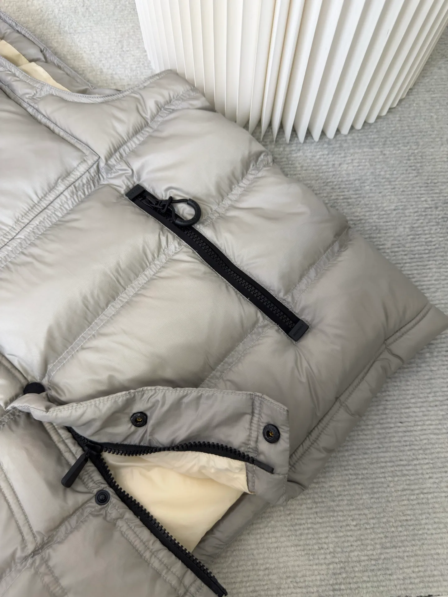 P700 MONCLER masked down vest with reflective markings is made of 90 white duck down with a weight of 130g to ensure excellent thermal insulation performance. After strict screening and processing, the velvet is not easy to get drilled, ensuring durability.  It is made of extremely fine nylon yarn and is woven in a high-density manner. The number of yarns per unit area is large, and the gaps between the yarns are very small, which can effectively block the penetration of cold wind. The fine weave keeps it lightweight and soft to the touch, physically restricting the lightweight down fibers from slipping through the gaps. Nylon fiber itself has good wear resistance and is not easy to snag, which significantly extends its service life and can easily cope with the needs of multiple scenarios.  The lining is made of high-density weaving of 100% polyester fiber, with a thickness of 0.08mm to avoid increasing the overall weight and making it smooth to wear. The high-density weaving structure forms a wind resistance layer to protect the thermal efficiency of the thermal layer from loss. It can withstand the expansion pressure of down and prevent deformation and damage after long-term use.  Through the reflective cloth punching process, the logo is regularly arranged on the triangular reflective mark with dozens of small holes, which not only improves functionality but also enhances recognition and aesthetics. Size 1 2 3 4