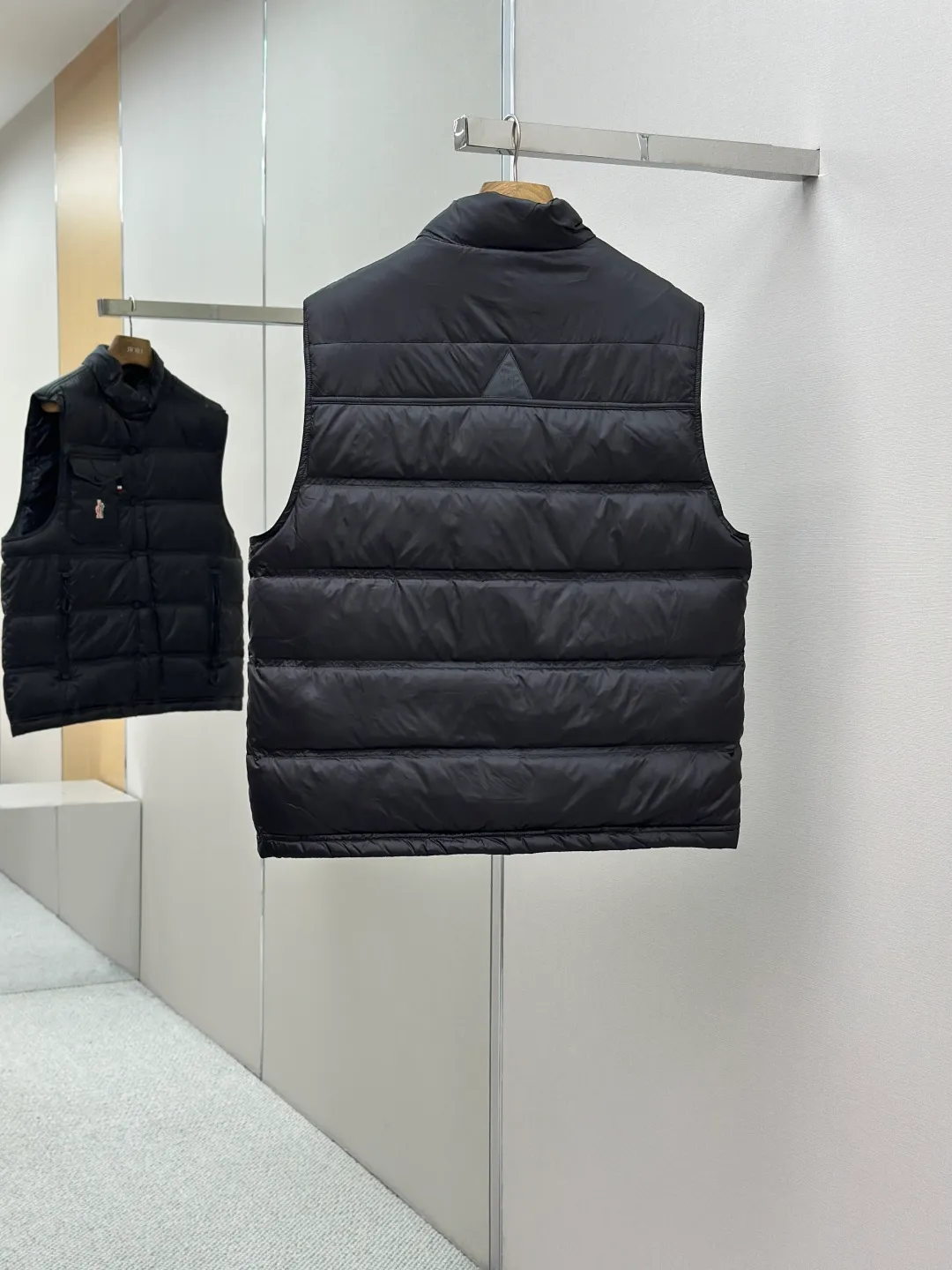 P680 MONCLER down vest with reflective markings Fabric selection: Made of ultra-fine nylon yarn woven in a high-density manner. The number of yarns per unit area is large, and the gaps between the yarns are very small, which can effectively block the penetration of cold wind. The fine weave keeps it lightweight and soft to the touch, physically restricting the lightweight down fibers from slipping through the gaps. Nylon fiber itself has good wear resistance and is not easy to snag, which significantly extends its service life and can easily cope with the needs of multiple scenarios.  Lining selection: The lining is made of 100% polyester fiber high-density weaving. The thickness of 0.08mm avoids increasing the overall weight and makes it smooth to wear. The high-density weaving structure forms a wind resistance layer to protect the thermal efficiency of the thermal insulation layer from loss. At the same time, it can withstand the expansion pressure of down and prevent deformation and damage after long-term use.  High-quality filling: 90 white duck down is selected, with a weight of 130g, ensuring excellent thermal insulation performance. After strict screening and processing, the velvet is not easy to get drilled, ensuring durability.  Process: Through the reflective cloth punching process, the logo is regularly arranged on the triangular reflective mark with dozens of small holes, which not only improves the functionality, but also strengthens the recognition and aesthetics.   Accessories: Customized snap buttons, customized zipper pullers, customized badges, customized elastic buckles, etc. SIZE: 1 2 3 4