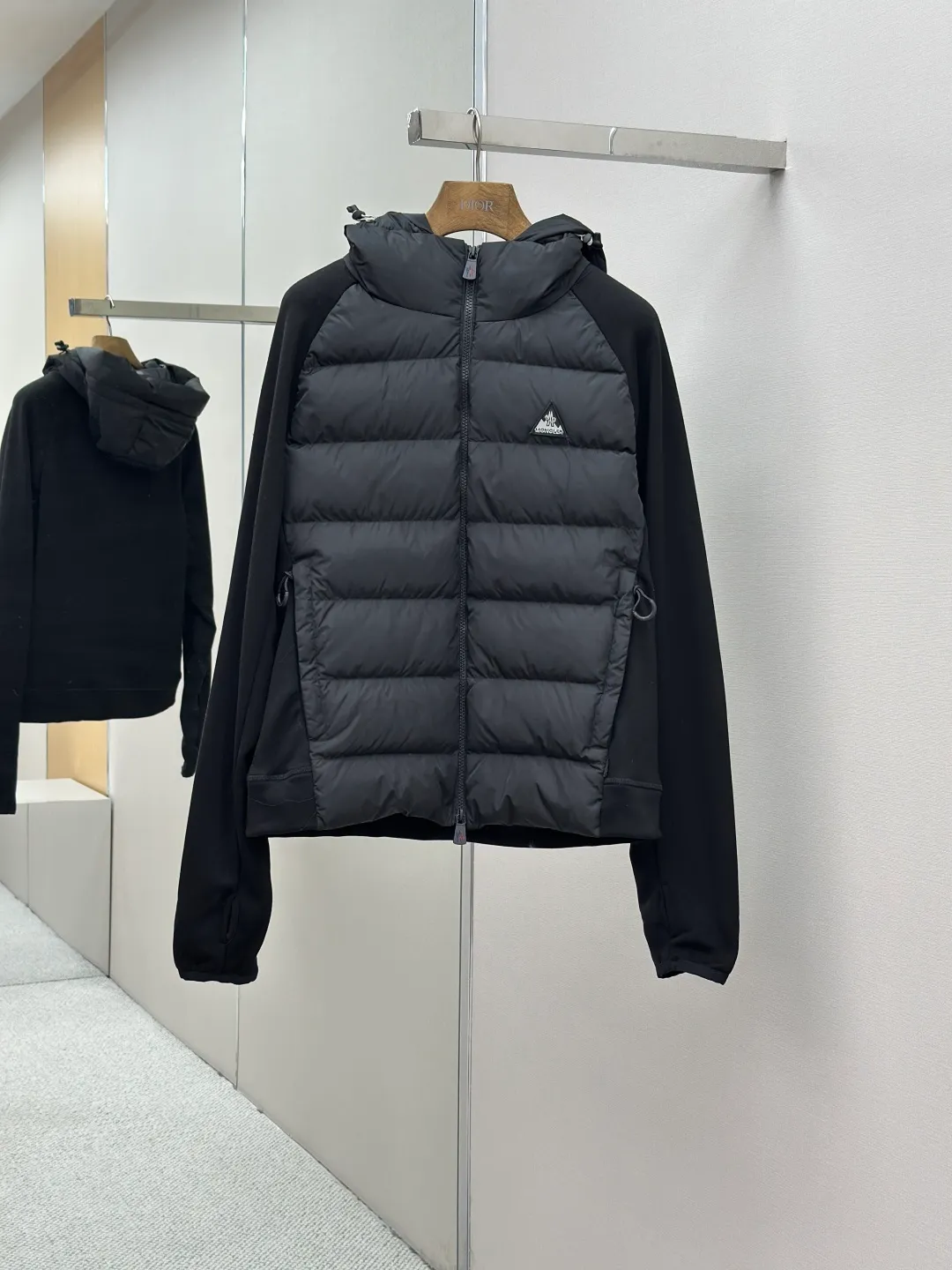 P810 Moncler logo woven splicing down jacket, customized matte crystal lattice air shield velvet and 300D high-density calendered coating, using the new national standard 90 white duck down (welcome to test), full of down, full of warmth, light and fluffy, with the dark green of the overlapping mountains as the background color, all things accumulating, creating its own scenery in silence The Monlcer triangle logo is embellished on the chest, the power aesthetics of the minimalist logo The concentrated down filling in the front area creates dynamic insulation for the core heat dissipation zone of the human body. The hooded down is a moving warm flow barrier for the head and neck, forming a thermal energy circulation system with the front area. The elastic woven sleeves provide freedom of movement with a sense of compression, forming a relaxed and warm philosophy. The real high-end is to let function become the footnote of style. Process 1: Computer mechanical down filling. Prioritize the liner pattern by making a pattern to determine the down filling area and determine the weight of down per square meter according to the original three-dimensional effect. Thus, the amount of down filling for each cut piece is calculated. The computer down filling machine uses a digital weighing unit to achieve stable measurement. Process 2: 3D three-dimensional quilting technology. With the programming system of the CNC quilting machine, the down in different areas is accurately separated to ensure that the filling is evenly fixed after sewing and avoid agglomeration or displacement. Process 3: Computer template machine line running process. The computer template machine line line process shows extremely high neatness and smoothness. The craftsman's precise control of the size during the operation ensures that each line meets the design requirements. The lines of the entire template are smooth and unified, neat and beautiful. Process 4: Triple locking five-thread dense stitching process. Main seam locking + diagonal reinforcement + raw edge wrapping. Triple structure. Forming a three-dimensional protective net at the edge of the fabric to avoid stitch breakage. Paving materials: Customized Moncler zippers. Customized Moncler rope loops. Customized Moncler logo. Customized Moncler eyelets. Customized Moncler trademark. Size: S M L XL