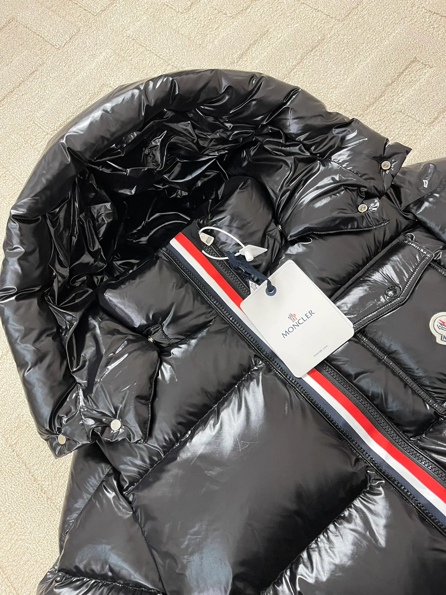 Flat detail P1180 Moncler Montbeliard glossy down jacket The Montbeliard down jacket is made of shiny patented nylon and features highly recognizable rectangular quilting. Featuring a hooded design and signature patch pocket at chest.  Fabric: 100% nylon Filling content: 90% white goose down 250-300g Craftsmanship: Made of nylon laqué fabric Nylon laque lining Filled with down, detachable and adjustable hood with drawstring closure Built-in flap with webbing, black pocket details at the lower end Zipper closure Collar with snap buttons Zipper pockets Patch pockets with snap buttons Adjustable cuffs Adjustable elastic drawstring hem.  Size: 1 2 3 4 5 0548000