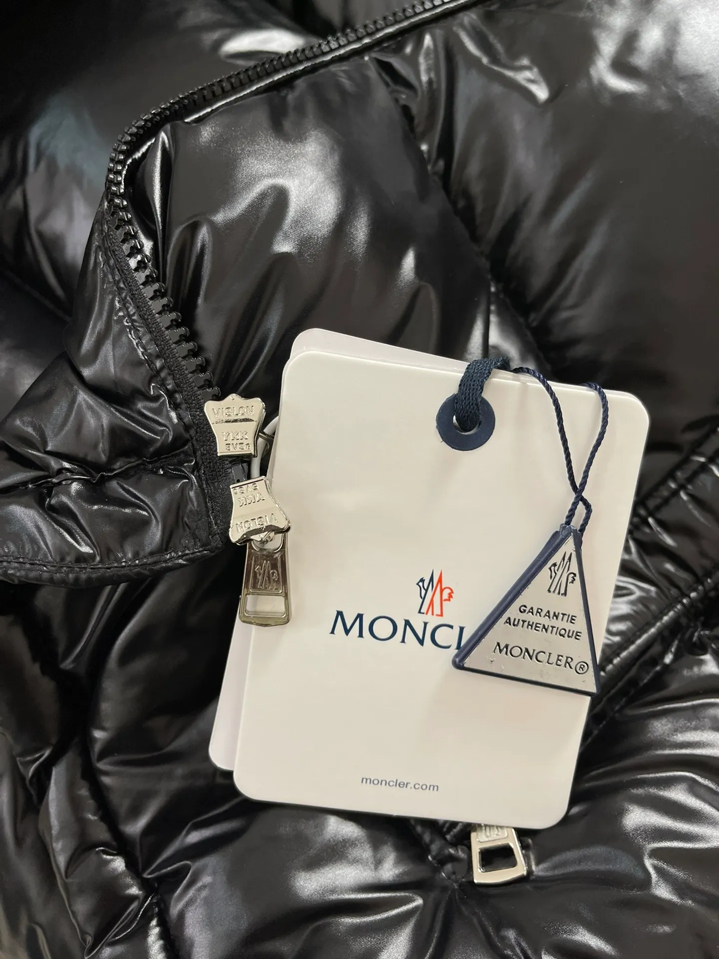 Flat detail P1180 Moncler Montbeliard glossy down jacket The Montbeliard down jacket is made of shiny patented nylon and features highly recognizable rectangular quilting. Featuring a hooded design and signature patch pocket at chest.  Fabric: 100% nylon Filling content: 90% white goose down 250-300g Craftsmanship: Made of nylon laqué fabric Nylon laque lining Filled with down, detachable and adjustable hood with drawstring closure Built-in flap with webbing, black pocket details at the lower end Zipper closure Collar with snap buttons Zipper pockets Patch pockets with snap buttons Adjustable cuffs Adjustable elastic drawstring hem.  Size: 1 2 3 4 5 0548000