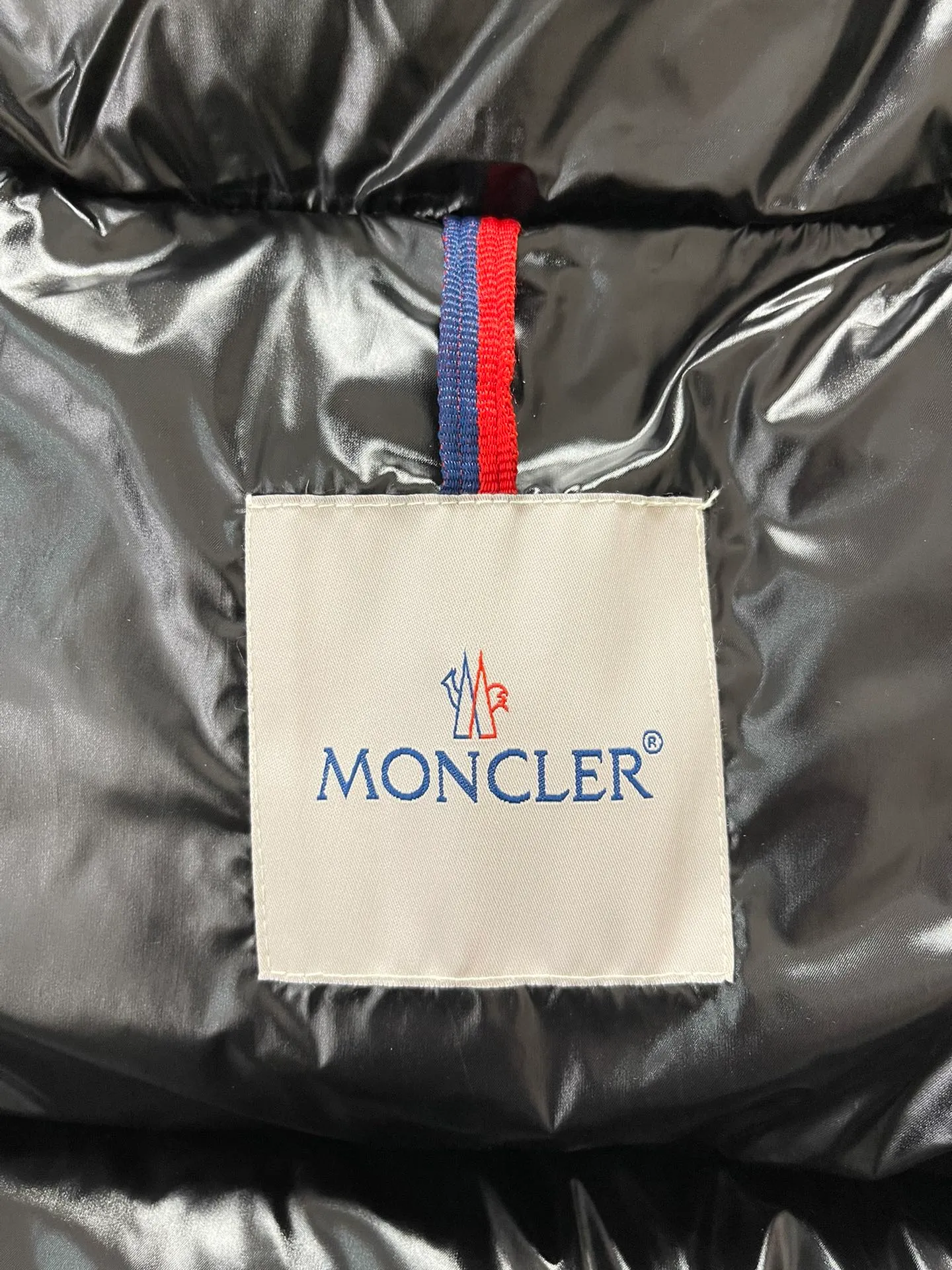 Flat detail P1180 Moncler Montbeliard glossy down jacket The Montbeliard down jacket is made of shiny patented nylon and features highly recognizable rectangular quilting. Featuring a hooded design and signature patch pocket at chest.  Fabric: 100% nylon Filling content: 90% white goose down 250-300g Craftsmanship: Made of nylon laqué fabric Nylon laque lining Filled with down, detachable and adjustable hood with drawstring closure Built-in flap with webbing, black pocket details at the lower end Zipper closure Collar with snap buttons Zipper pockets Patch pockets with snap buttons Adjustable cuffs Adjustable elastic drawstring hem.  Size: 1 2 3 4 5 0548000